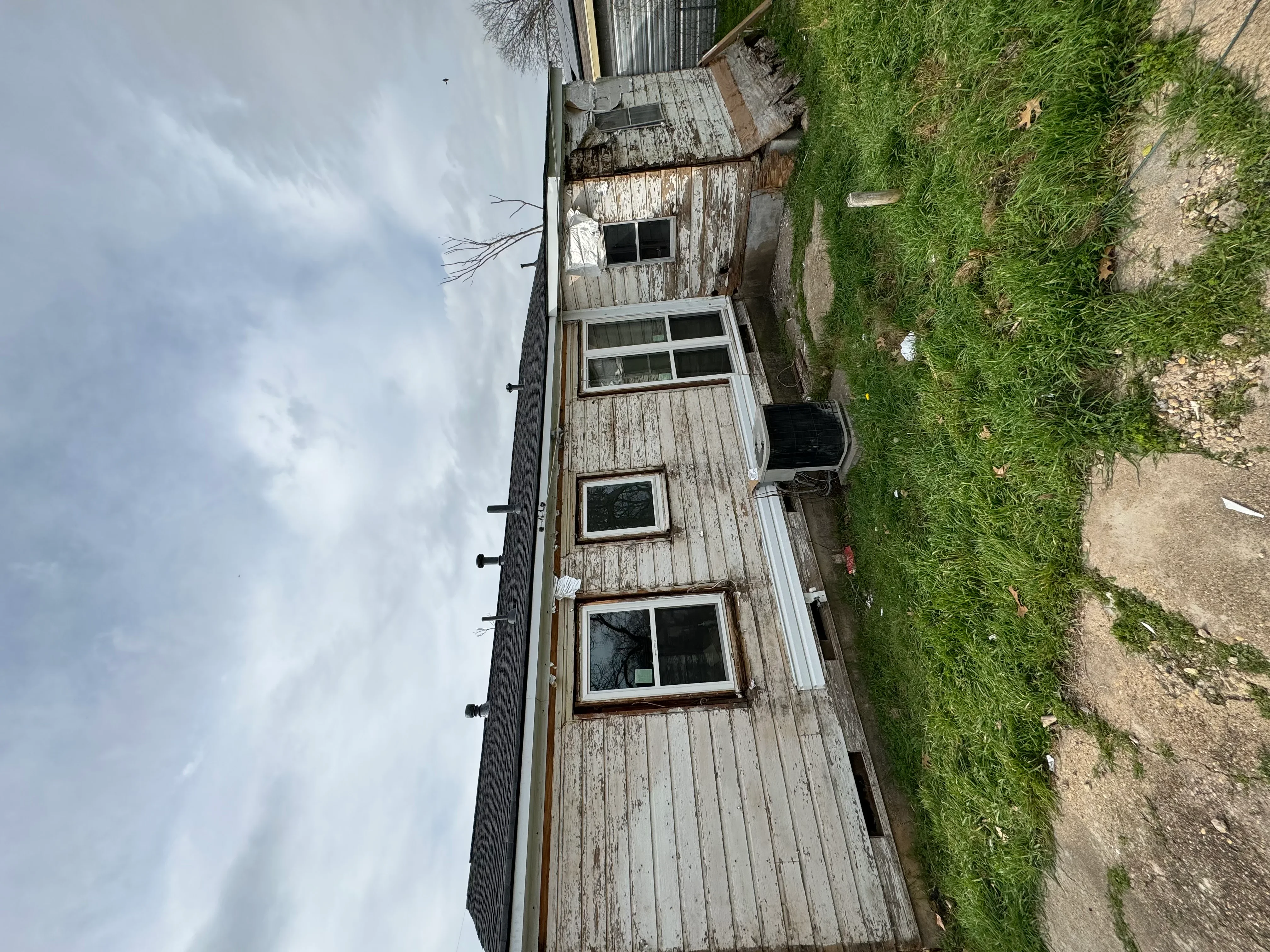 Weathered wood siding with multiple windows and deteriorated wood planking on residential structure
