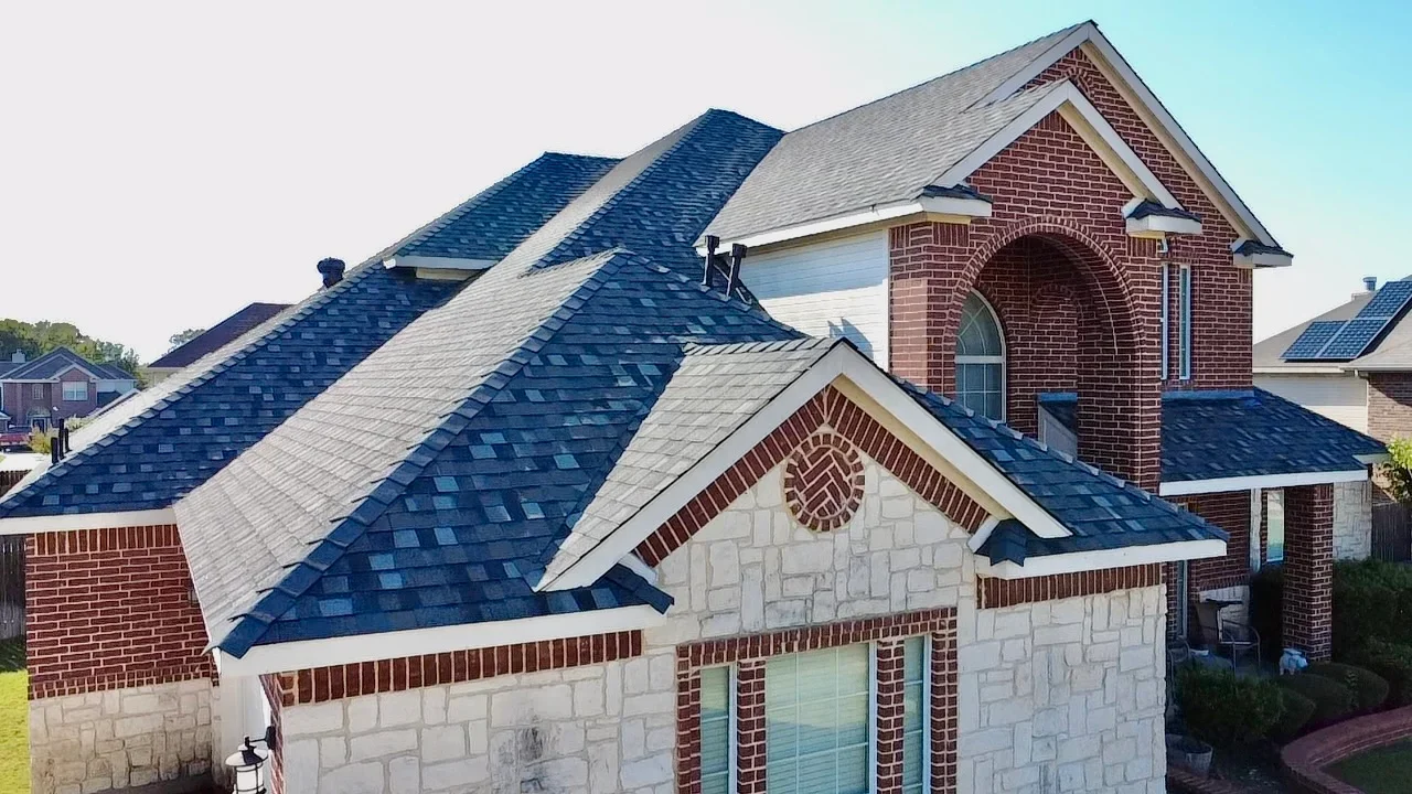 Multi-slope residential roof with blue and gray dimensional shingles, brick and stone exterior, multiple dormers and gables
