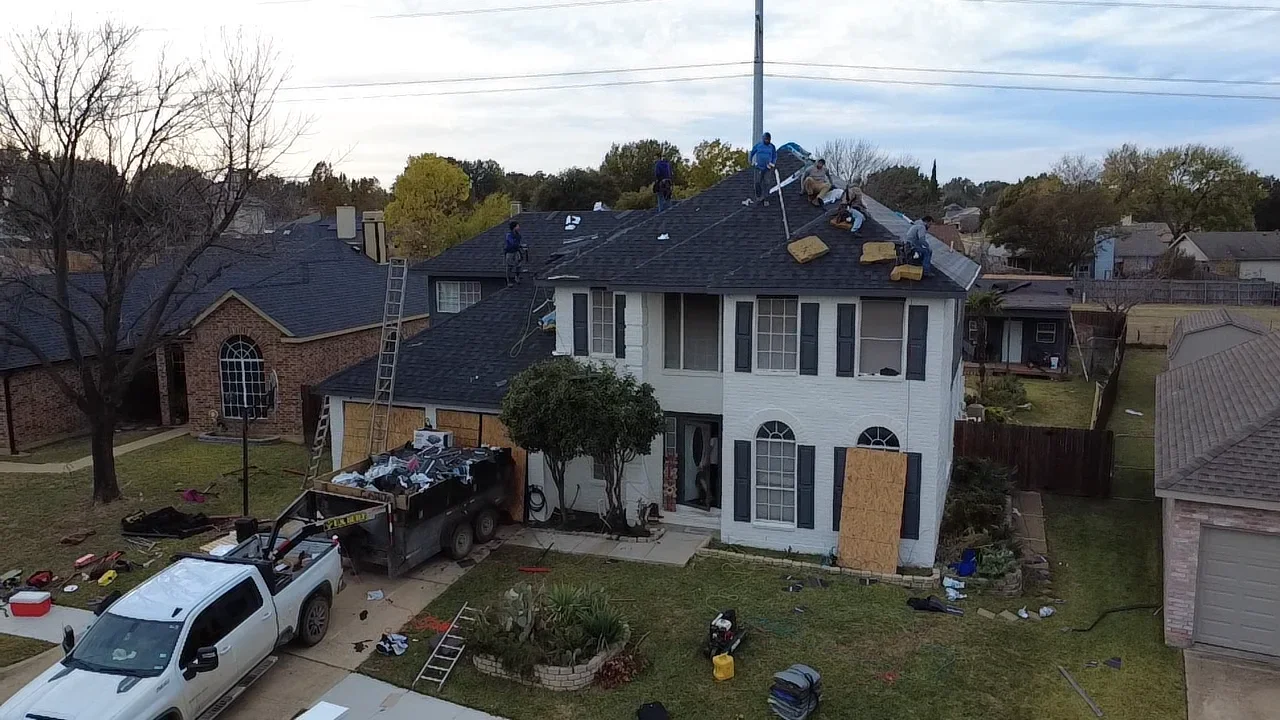 Two-story home with new asphalt shingle roof installation in progress, crew working on roof planes
