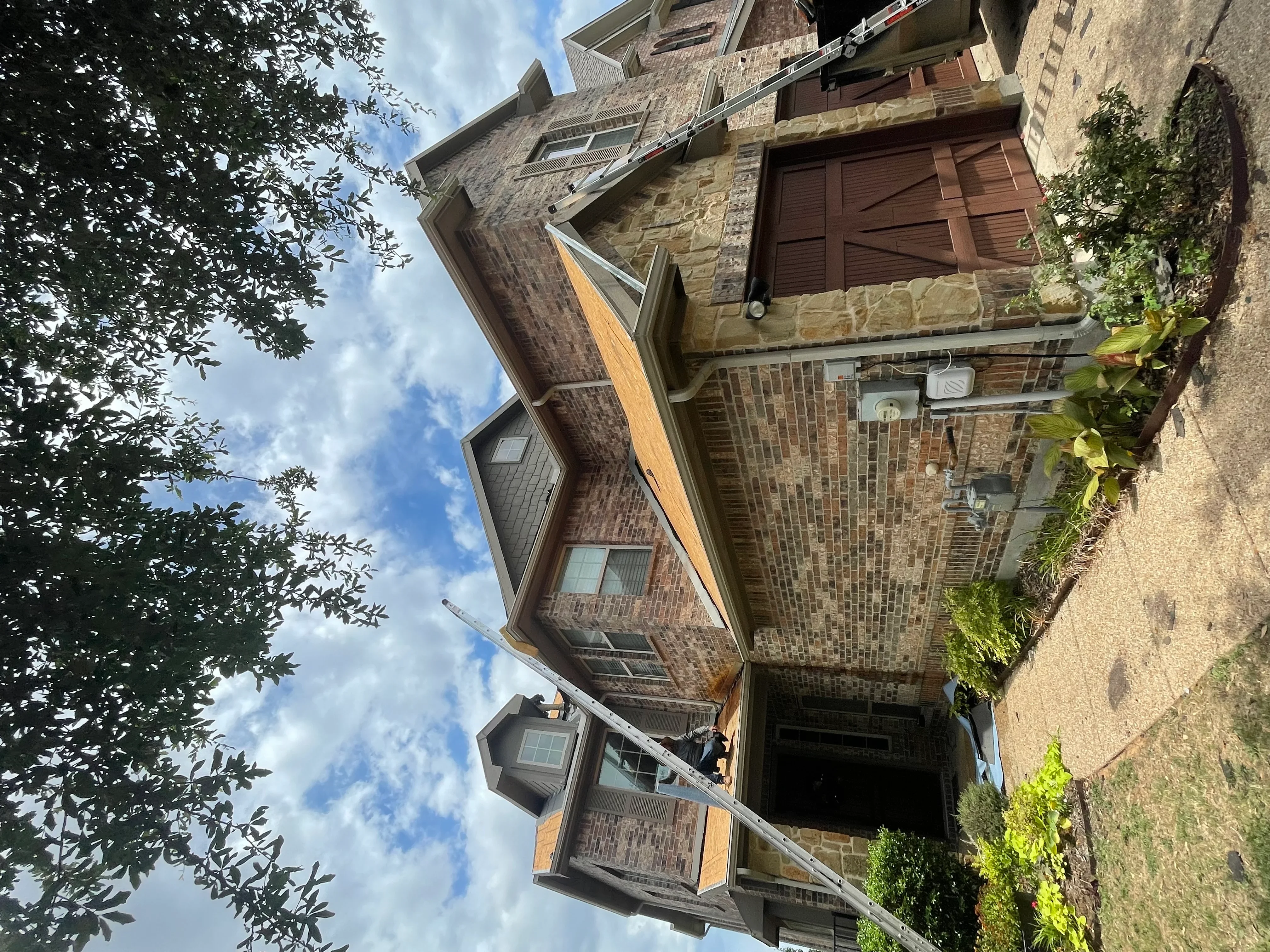 Multi-story stone and brick home with new roofing installation on complex rooflines and peaks