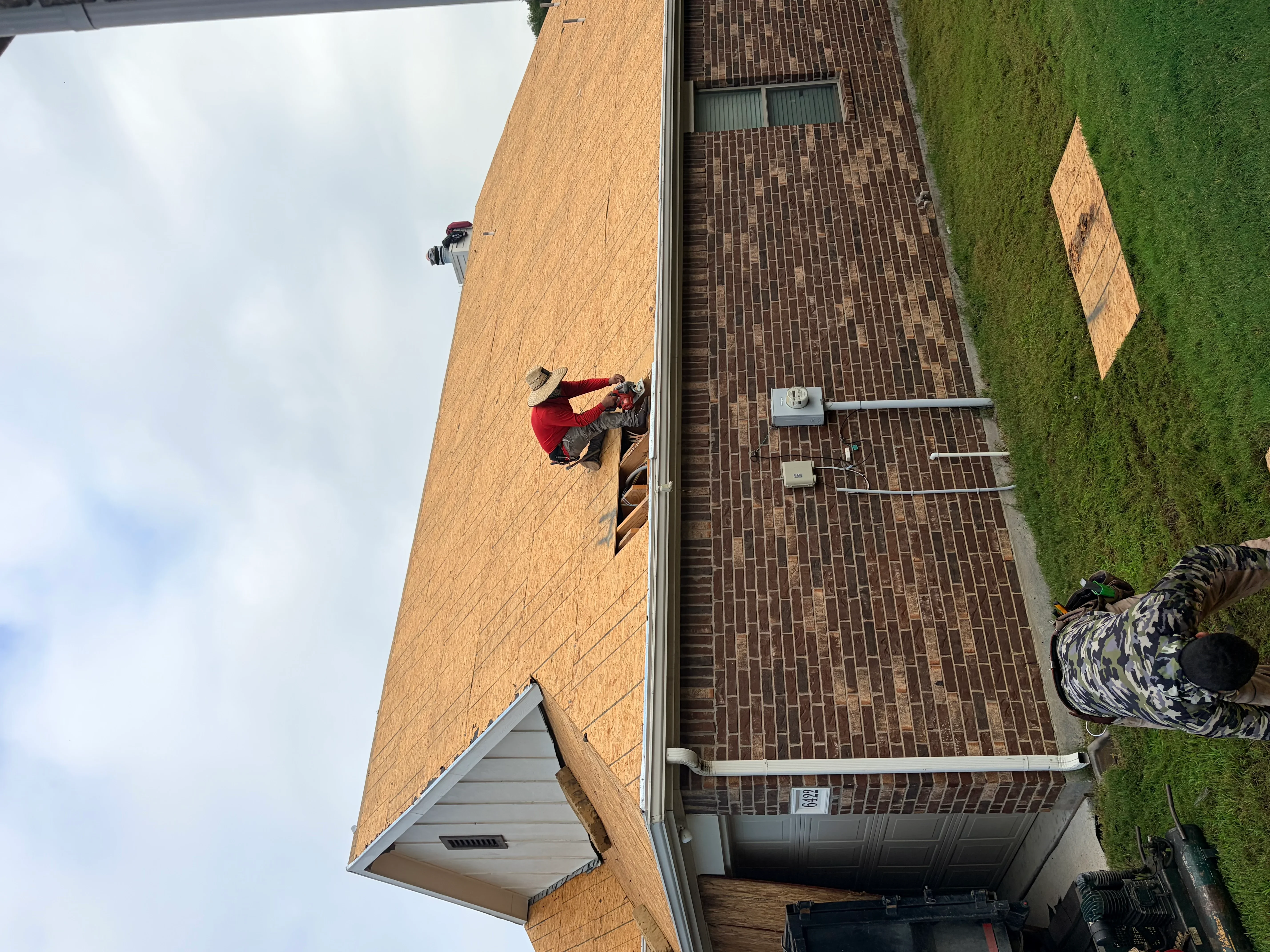 Roofer installing dark brown asphalt shingles on pitched brick home roof