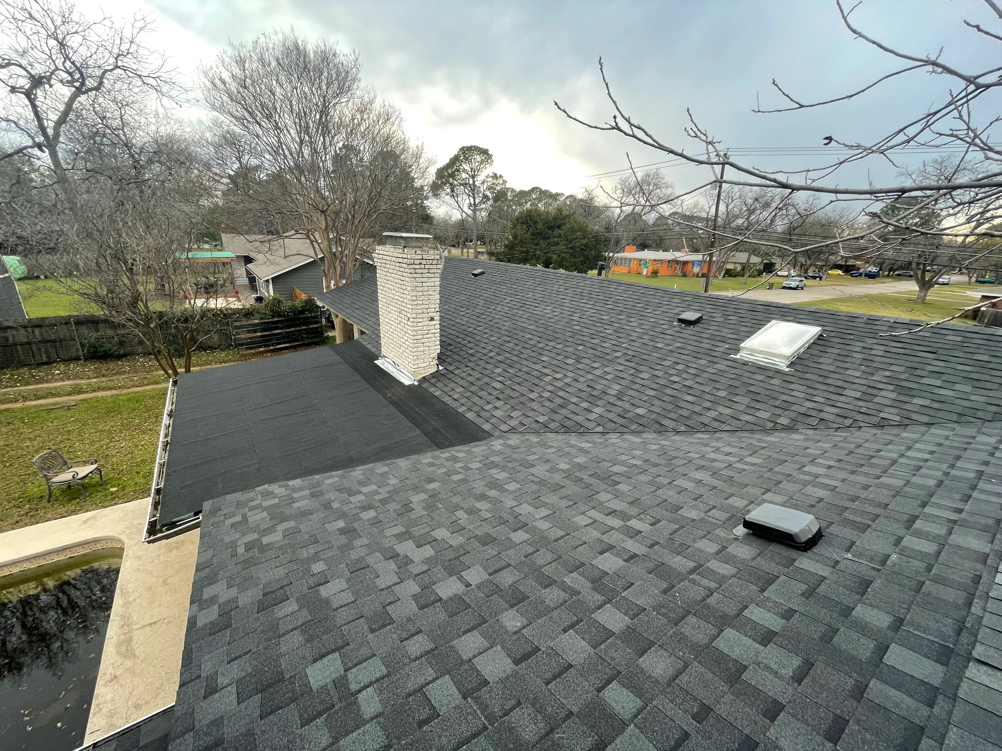 Charcoal gray architectural shingles on multi-plane residential roof with white brick chimney