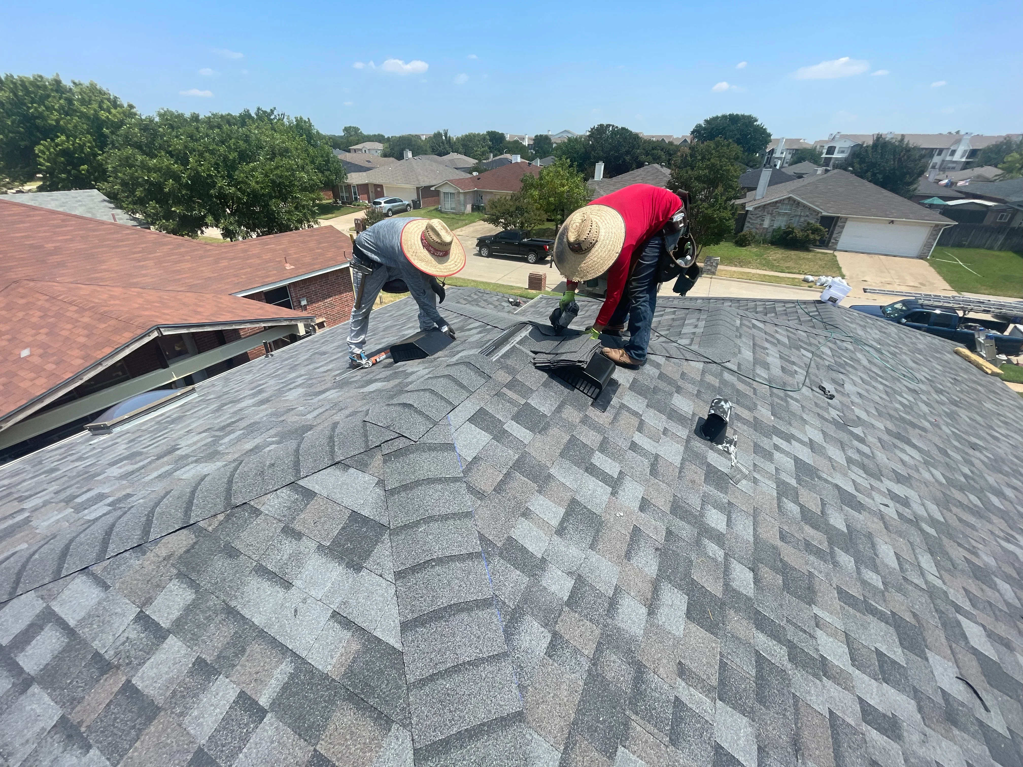Roofers installing gray architectural shingles on residential roof with staggered pattern