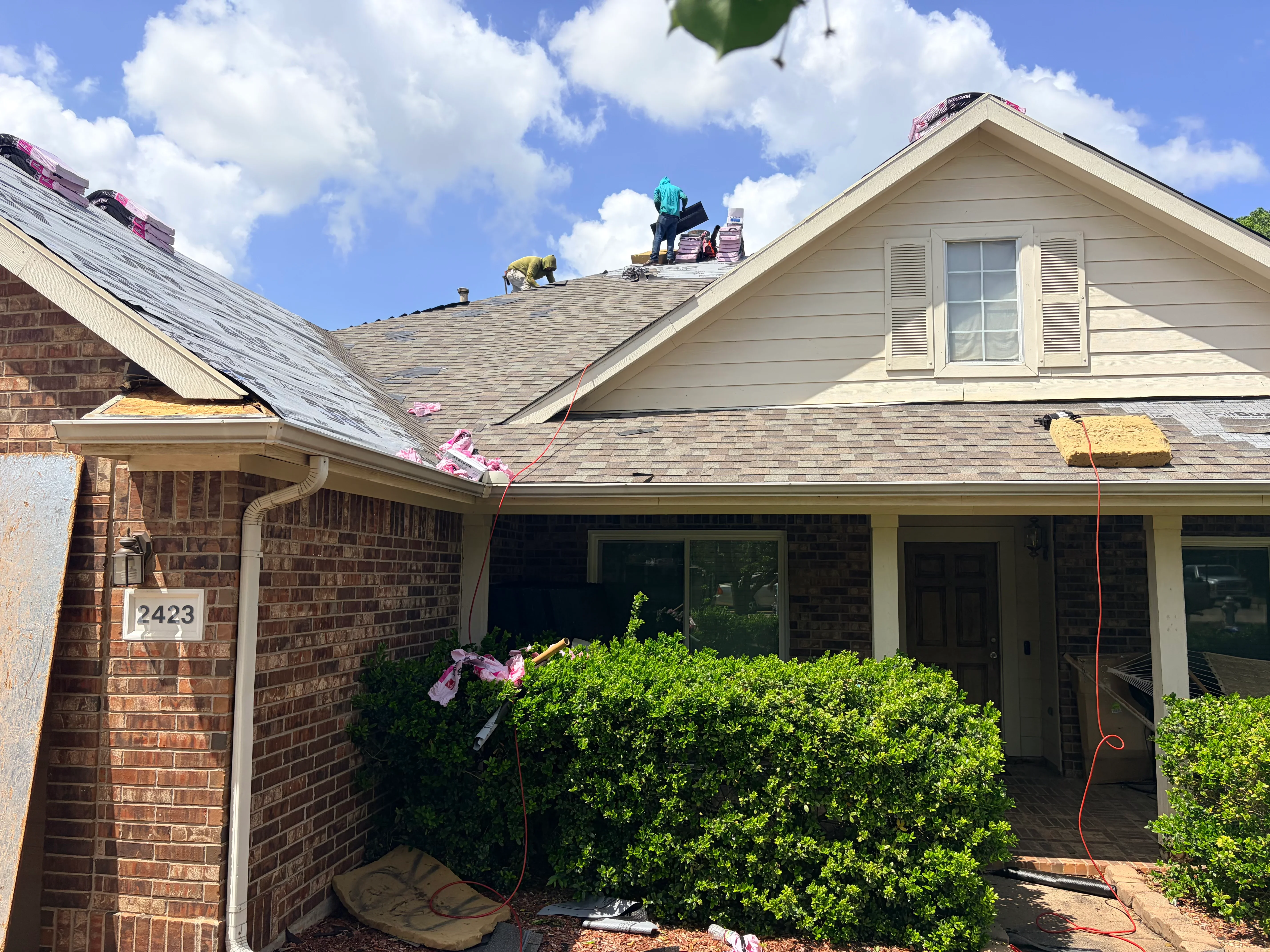 Roofers installing new asphalt shingles on residential home with brick exterior and gable roof