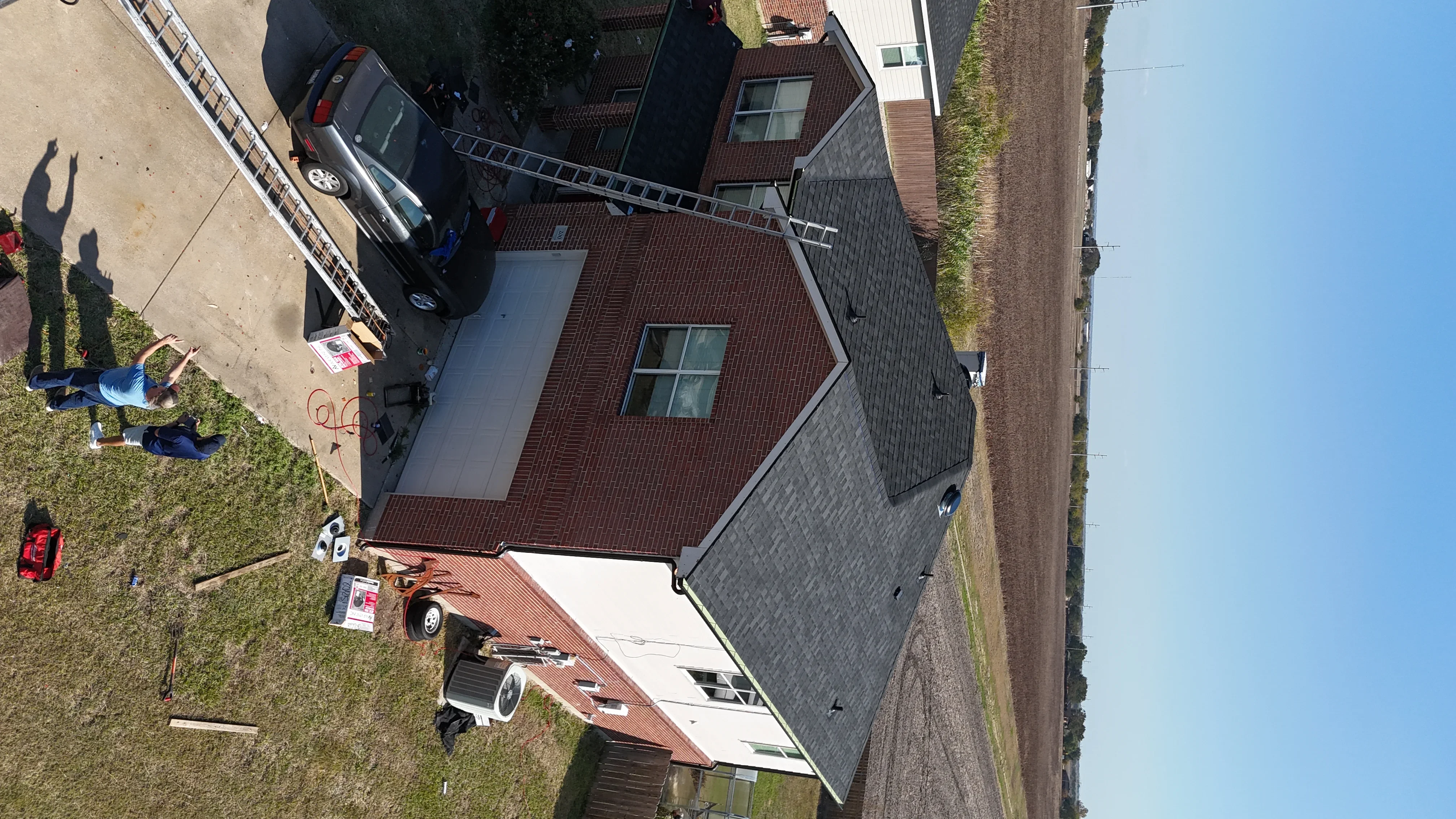 Aerial view of residential home with newly installed burgundy asphalt shingle roof and brick exterior