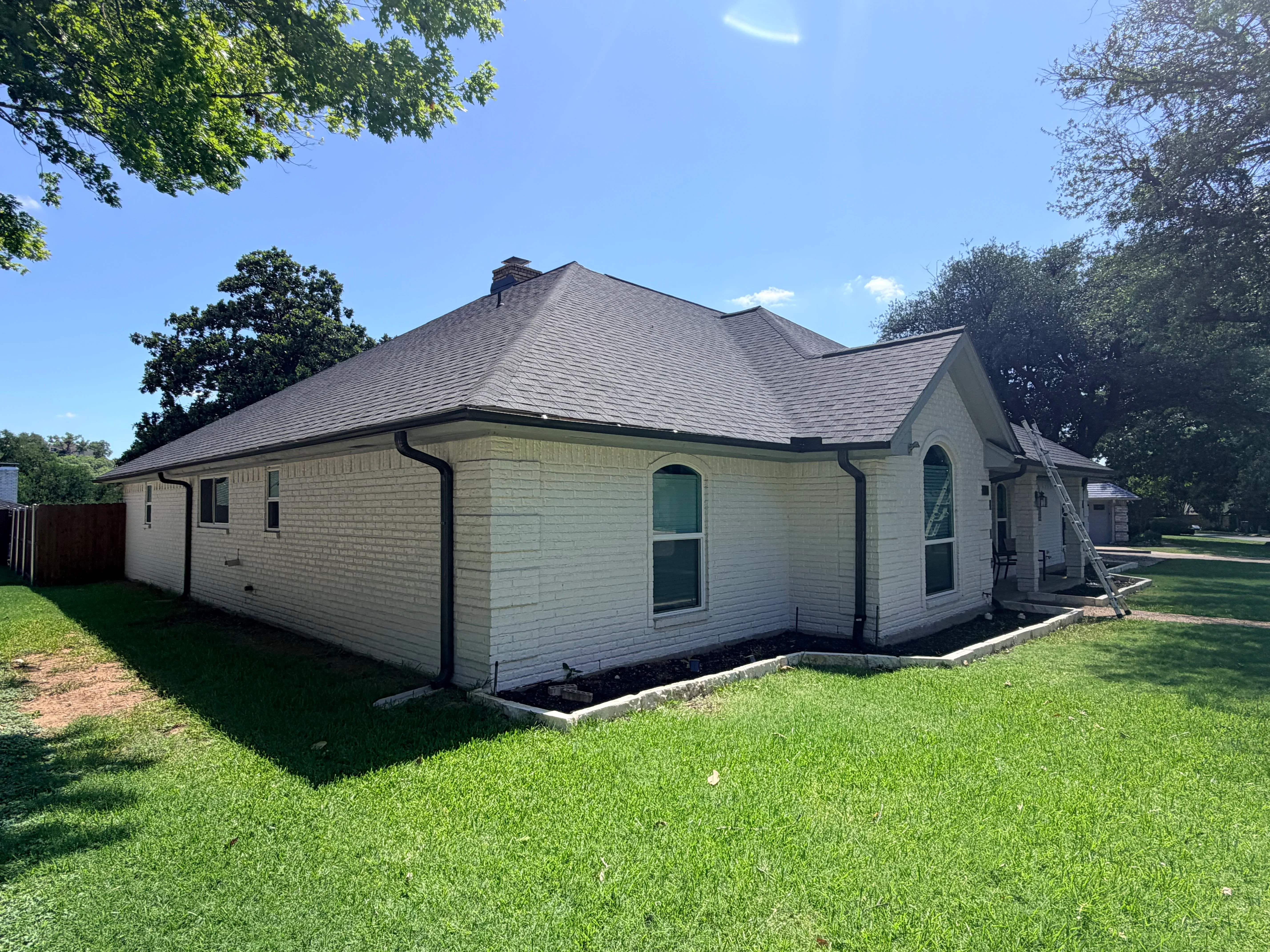 New charcoal gray asphalt shingle roof on white brick single-story home with black gutters