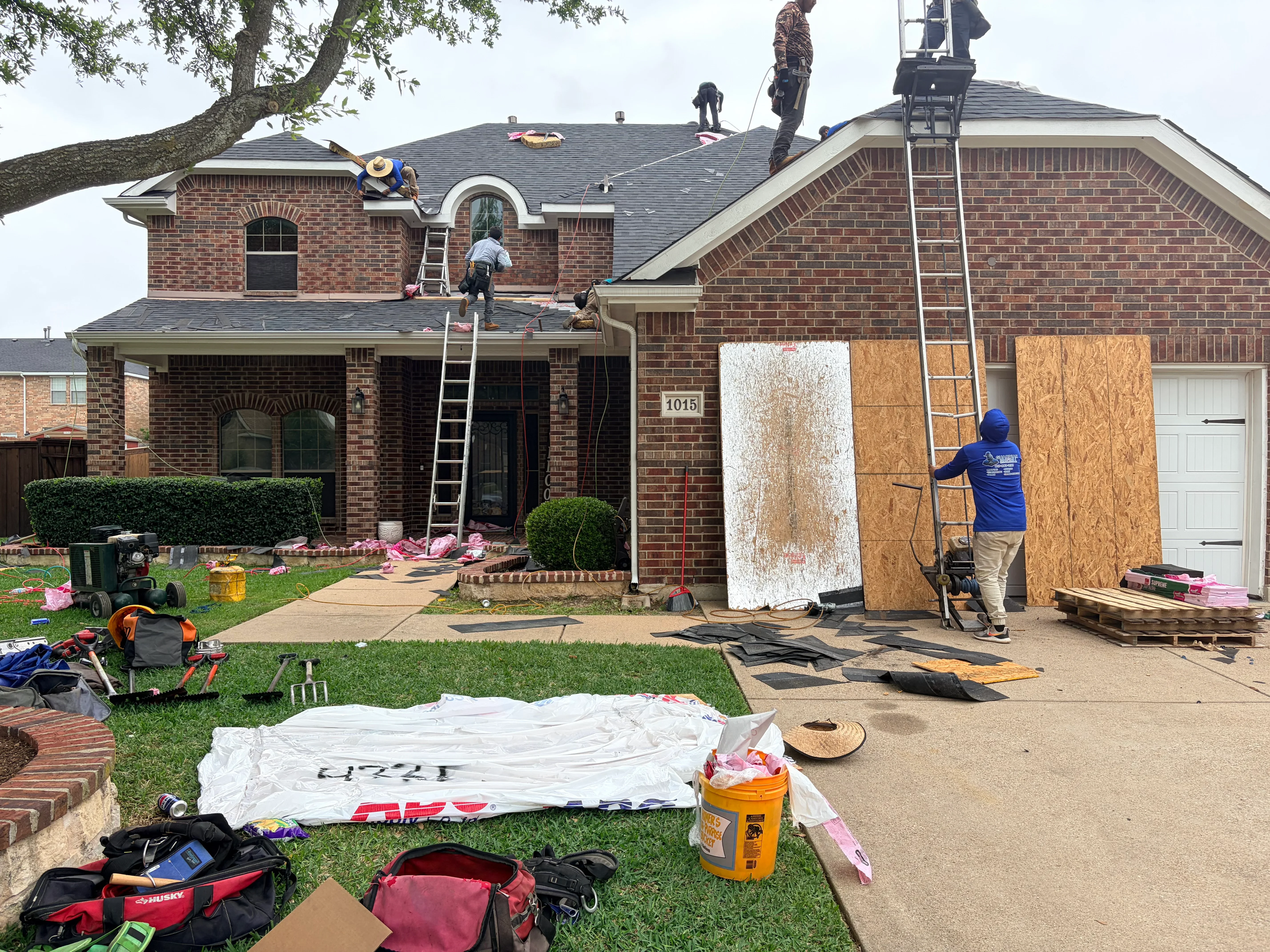 Roofers installing new architectural shingles on two-story brick home with multiple roof planes
