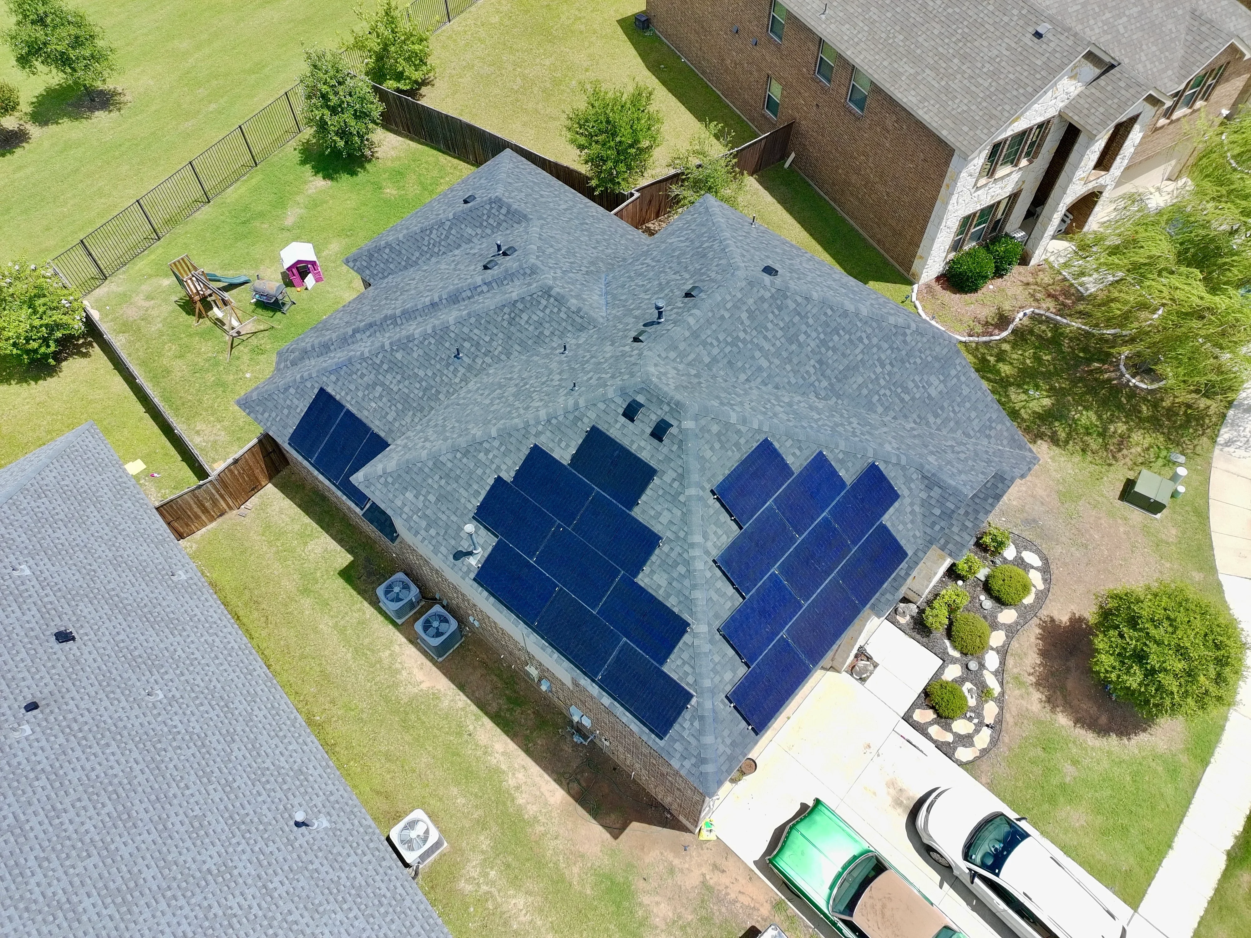 Aerial view of slate gray architectural shingle roof with dual solar panel arrays installed on residential home