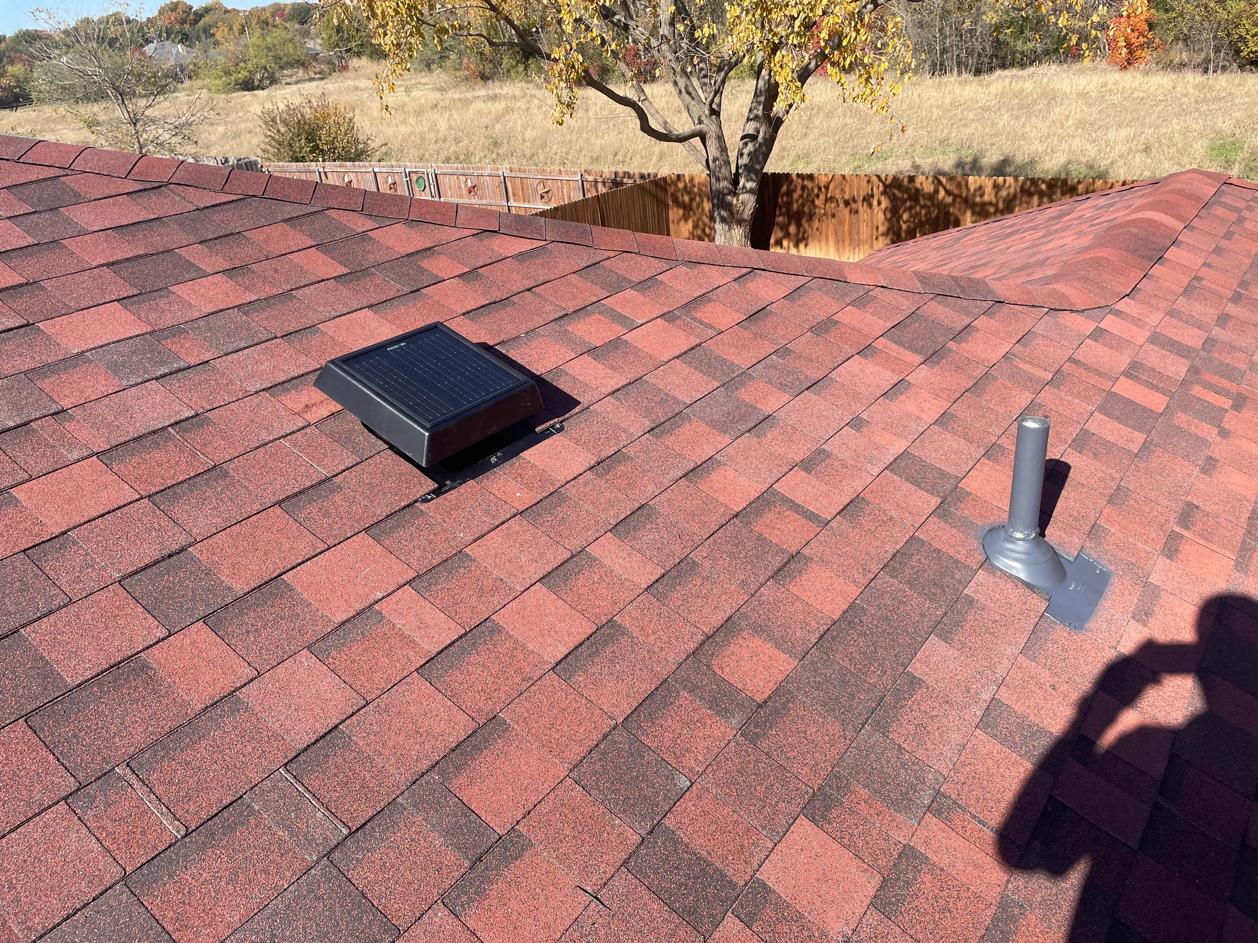 Red asphalt shingle roof with solar attic fan and metal vent pipe installed
