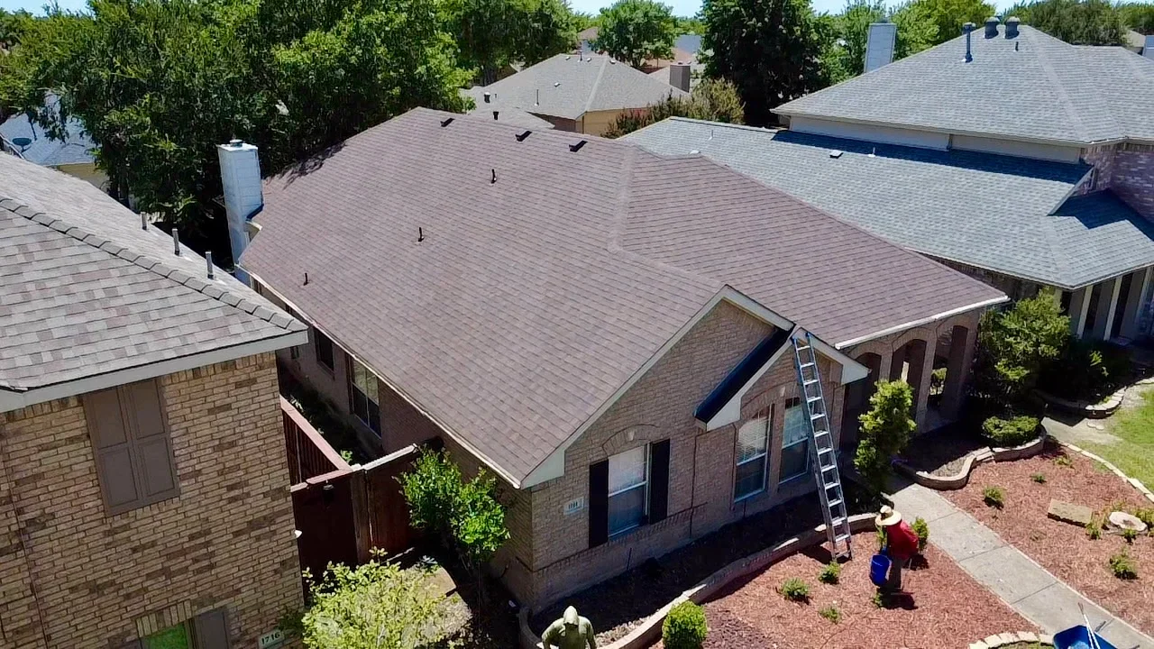 Newly installed brown architectural asphalt shingle roof on brick residential home with ladder and crew visible