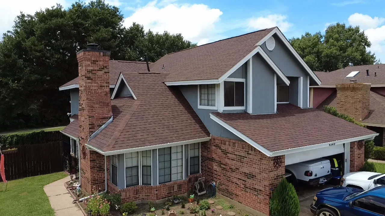 Two-story brick home with new brown architectural shingle roof, white gutters, and brick chimney