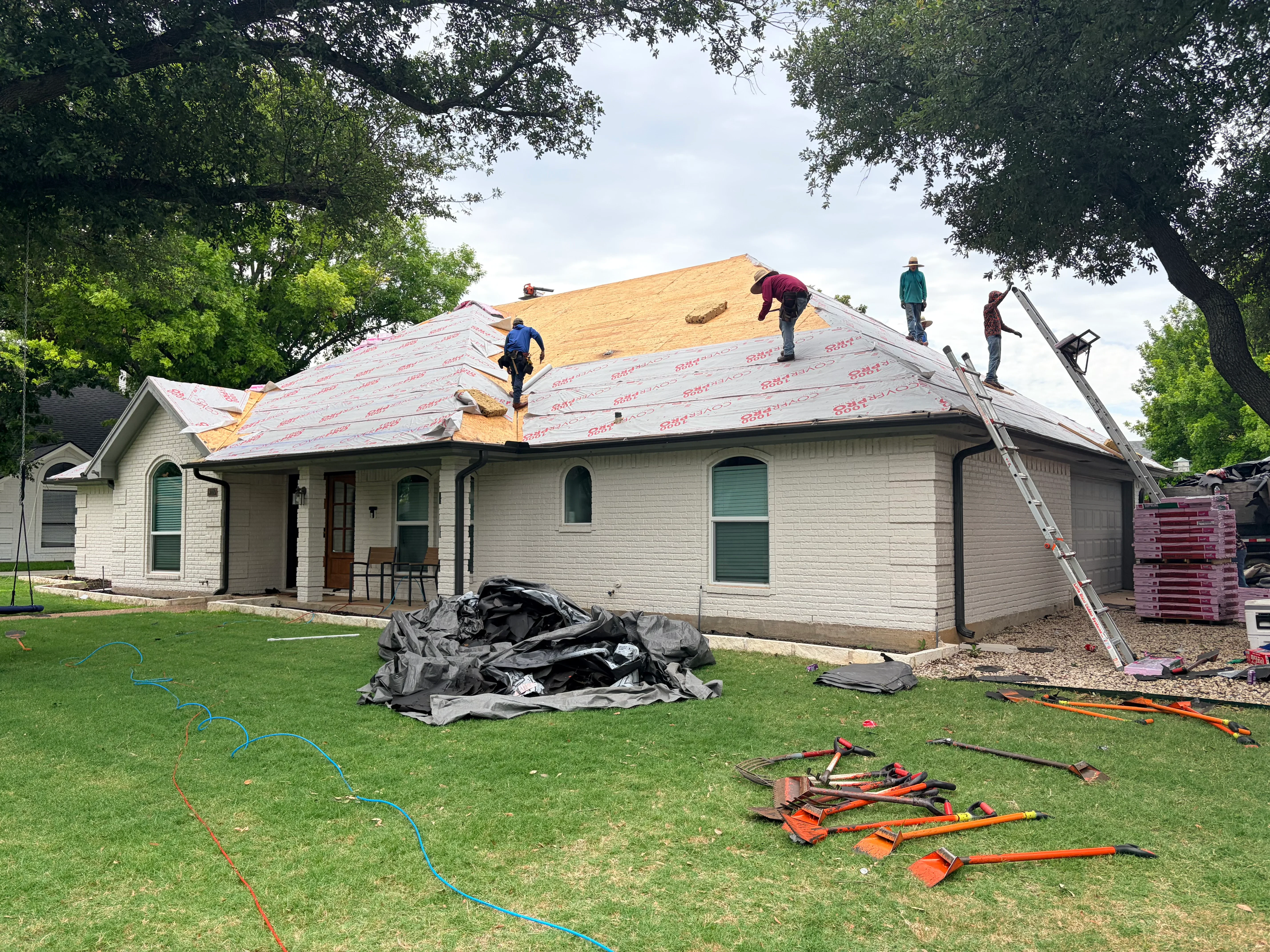 Roof replacement in progress with new sheathing and asphalt shingles on white brick home