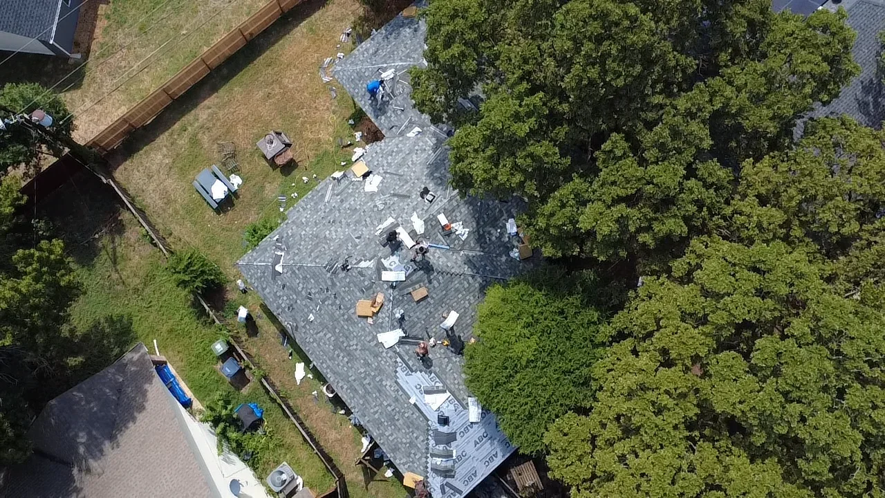 Aerial view of residential roof replacement with dark gray architectural shingles and installation crew
