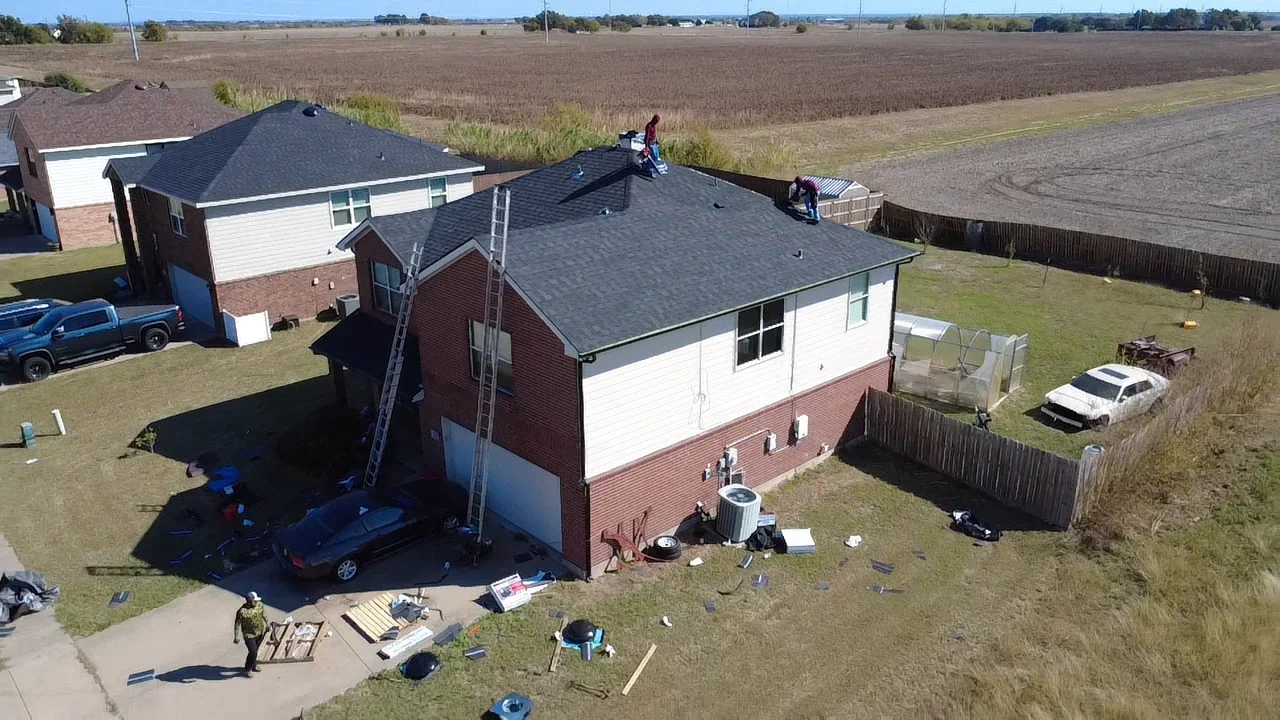 Dark asphalt shingle roof installation on brick residential home with crew and equipment