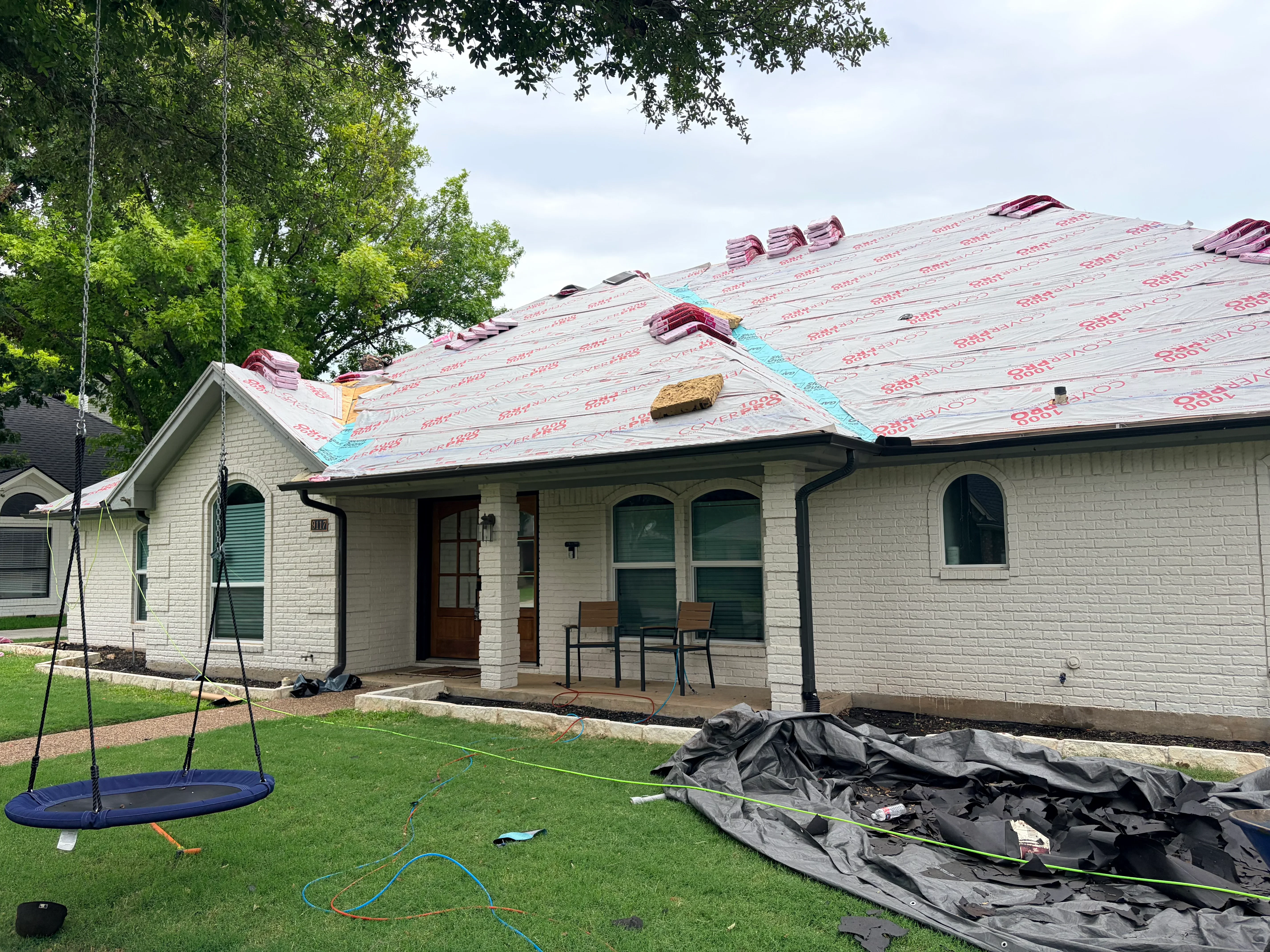 Roof replacement in progress with new sheathing, red underlayment, and burgundy shingles on brick home
