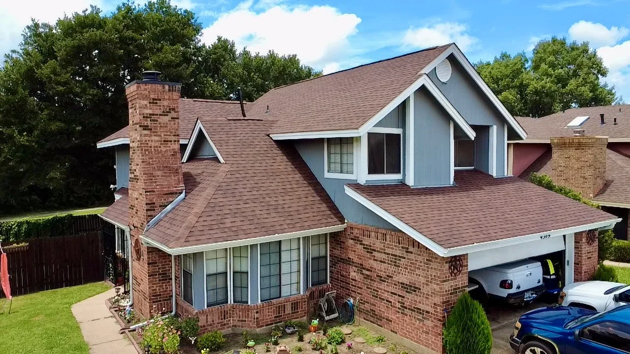 Brown architectural shingle roof on brick home with white trim and dormers