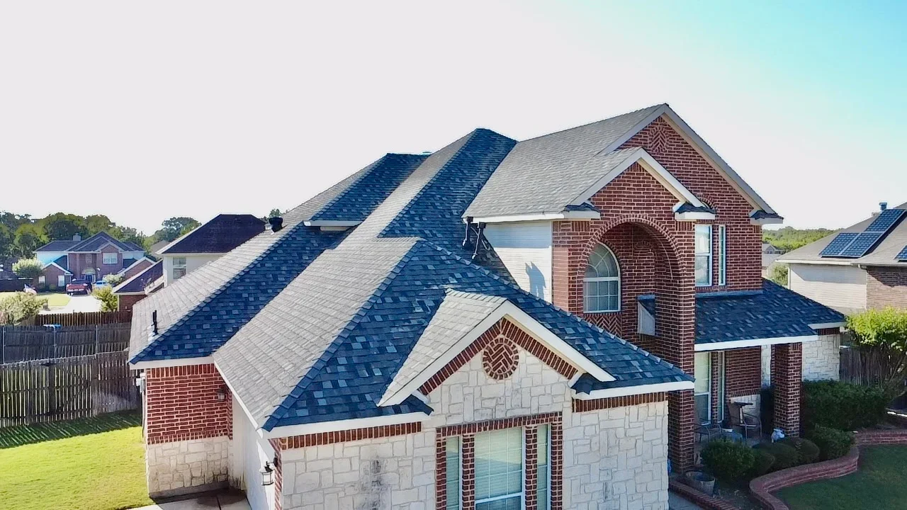 Multi-pitch residential roof with blue-gray architectural shingles, brick and stone exterior, dormers and valleys