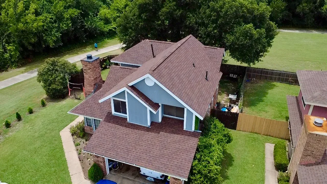 Burgundy architectural shingles on multi-peaked residential roof with white gable trim and carport