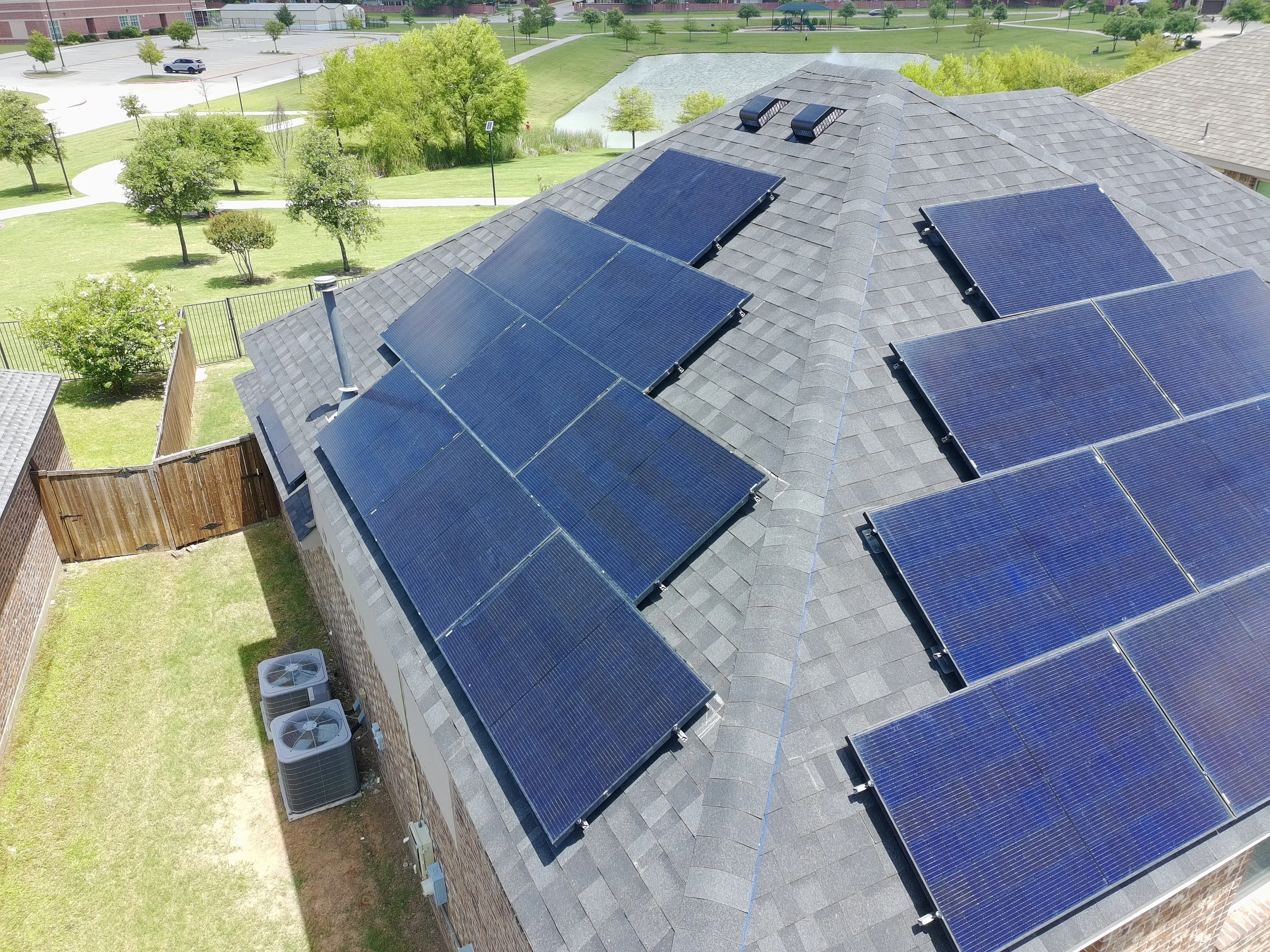 Aerial view of solar panel array installed on residential roof with black shingles and mounting hardware