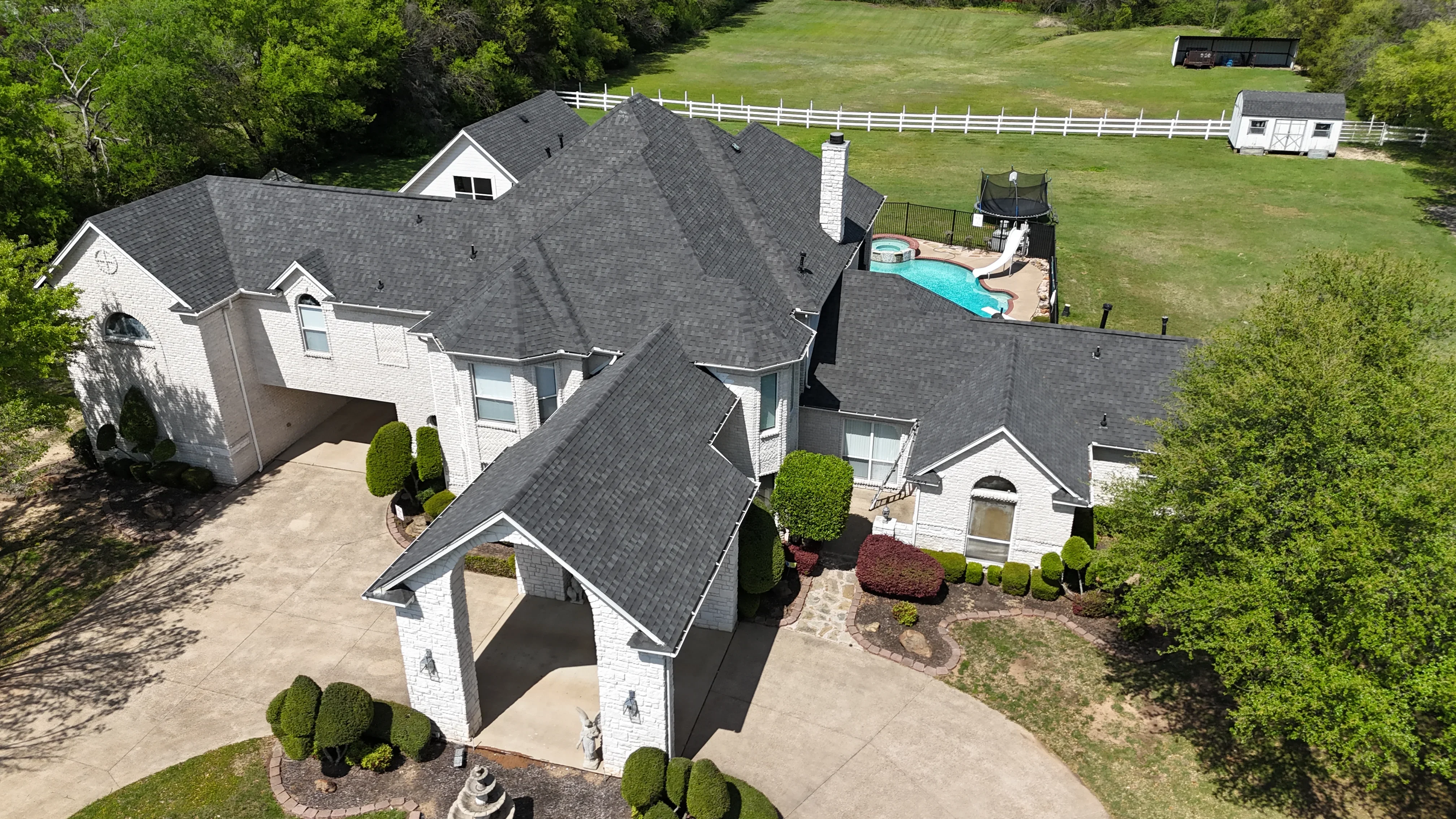 Charcoal gray architectural shingle roof on white brick two-story home with chimney and gable details