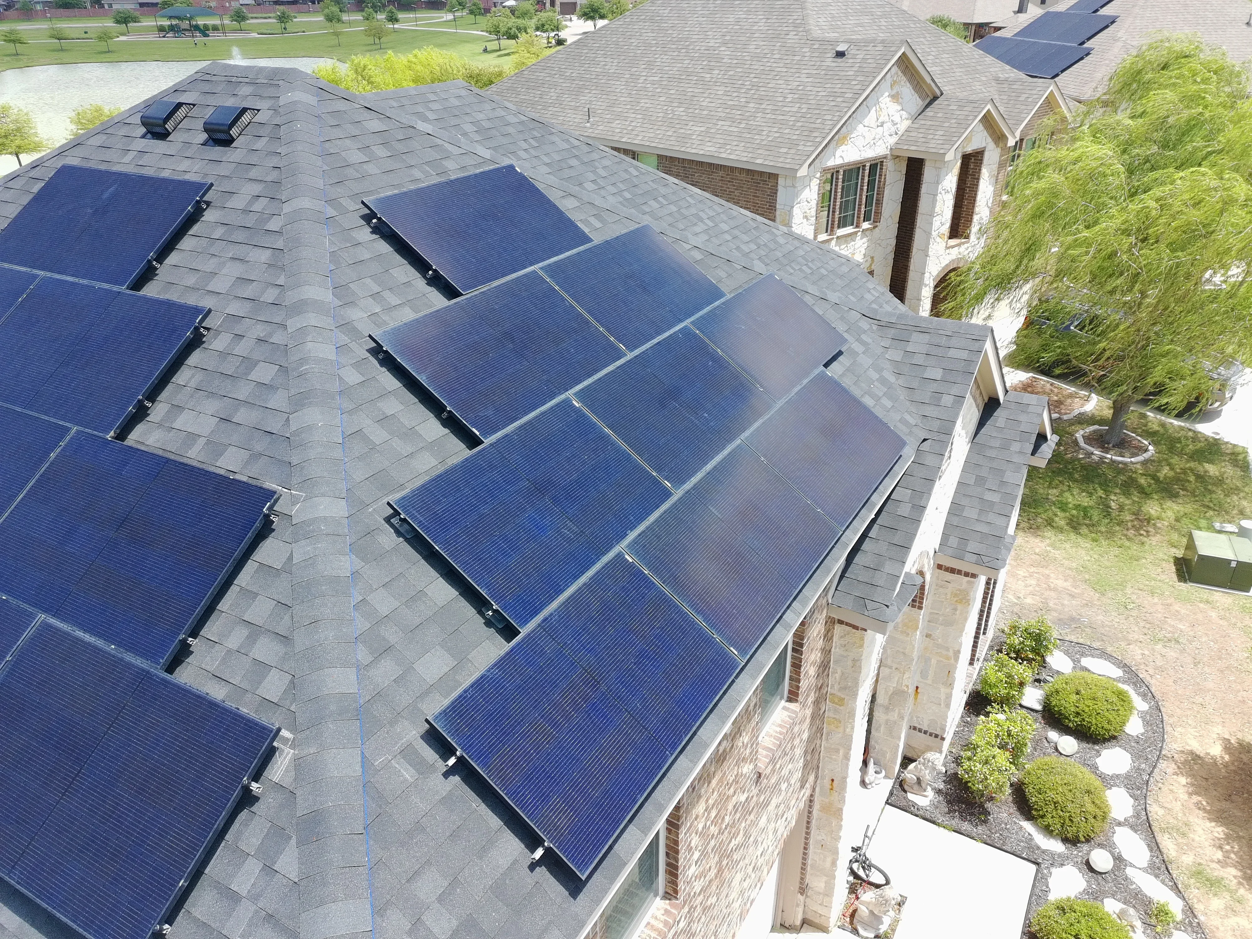 Aerial view of residential roof with blue solar panels mounted on gray architectural shingles