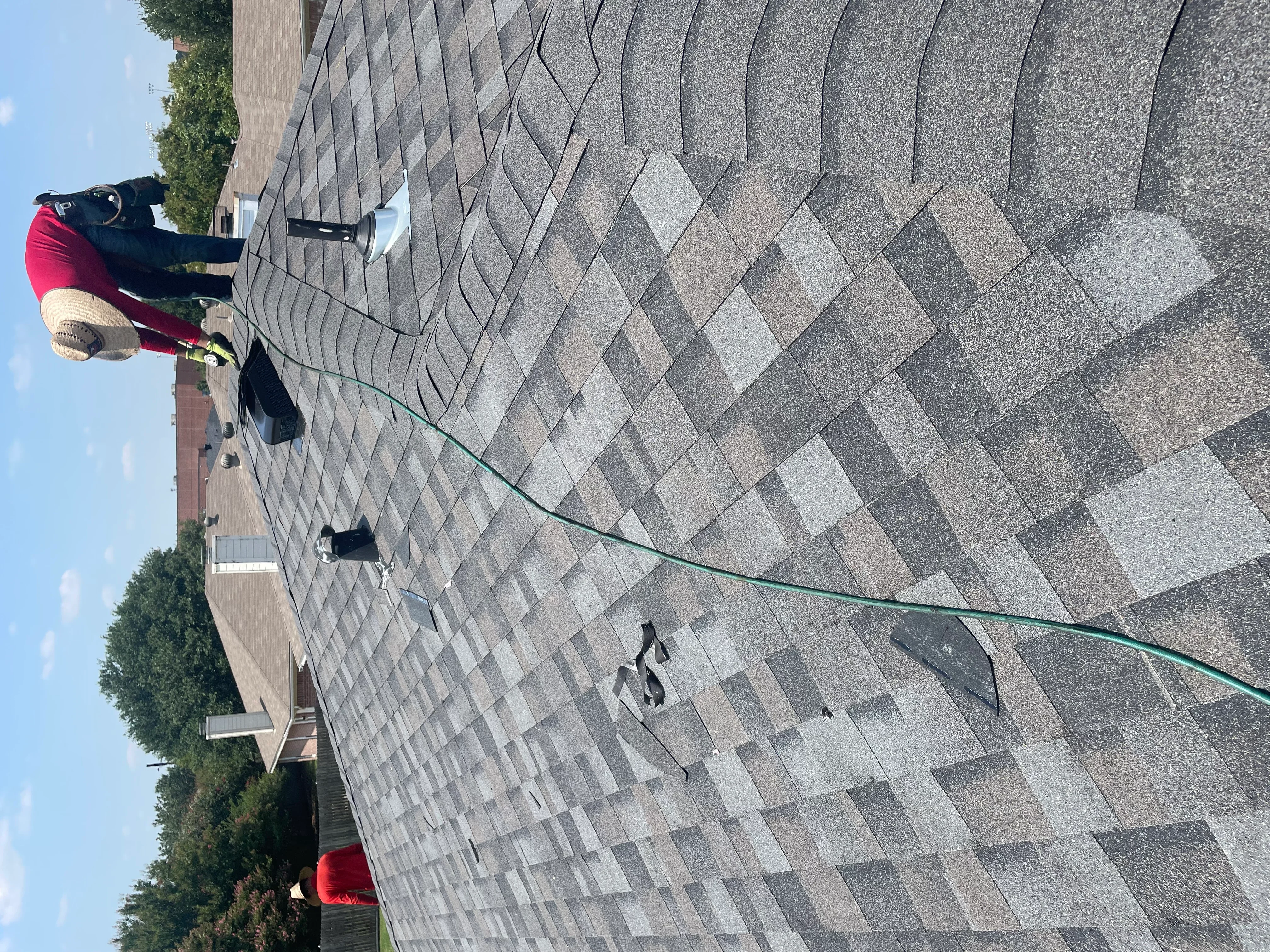 Worker installing gray asphalt shingles on residential roof with diamond pattern layout
