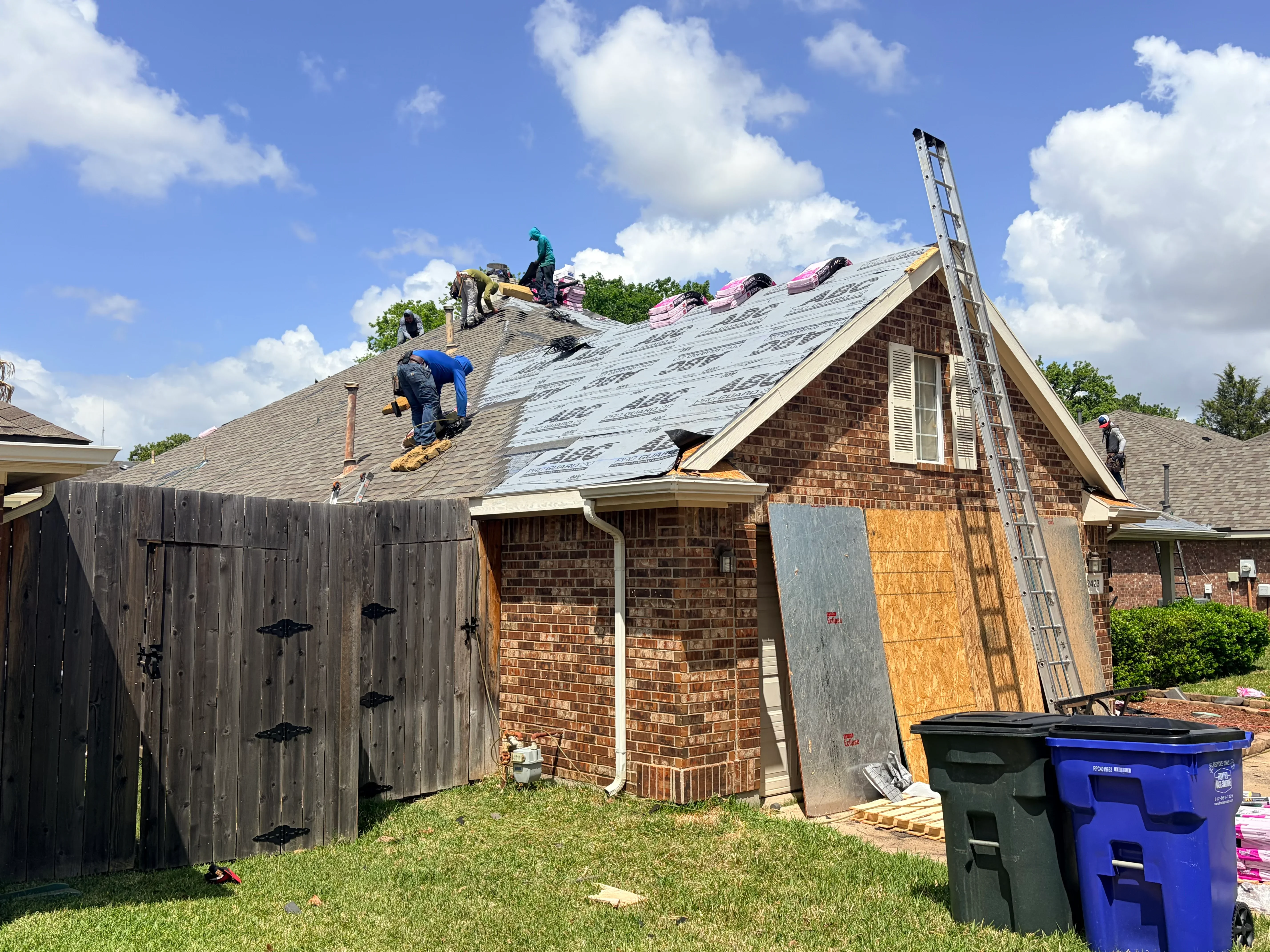 Roofers installing asphalt shingles on brick home with multi-pitched roof and dormer