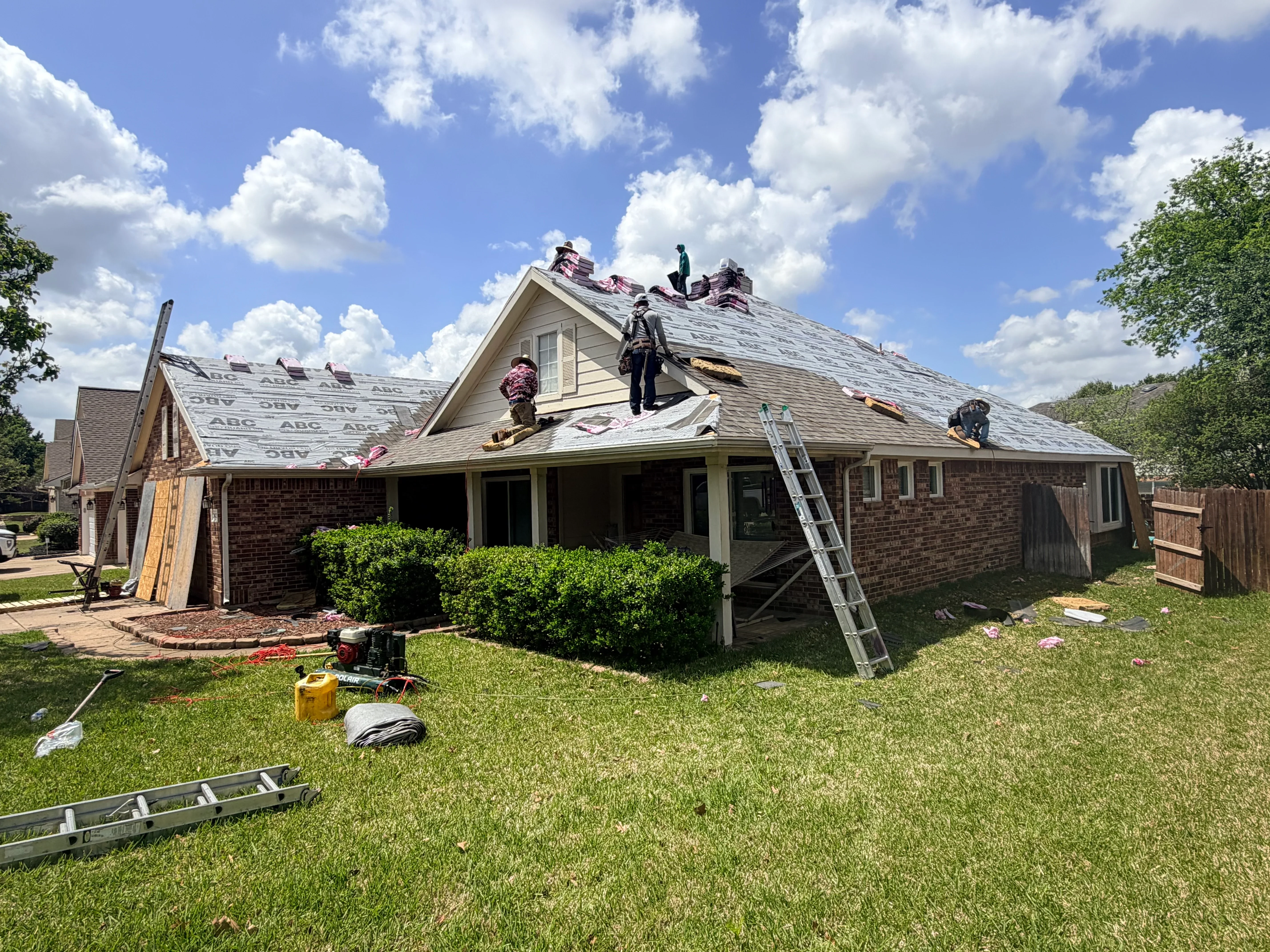 Roofers installing new shingles on brick home with multiple roof planes and chimneys