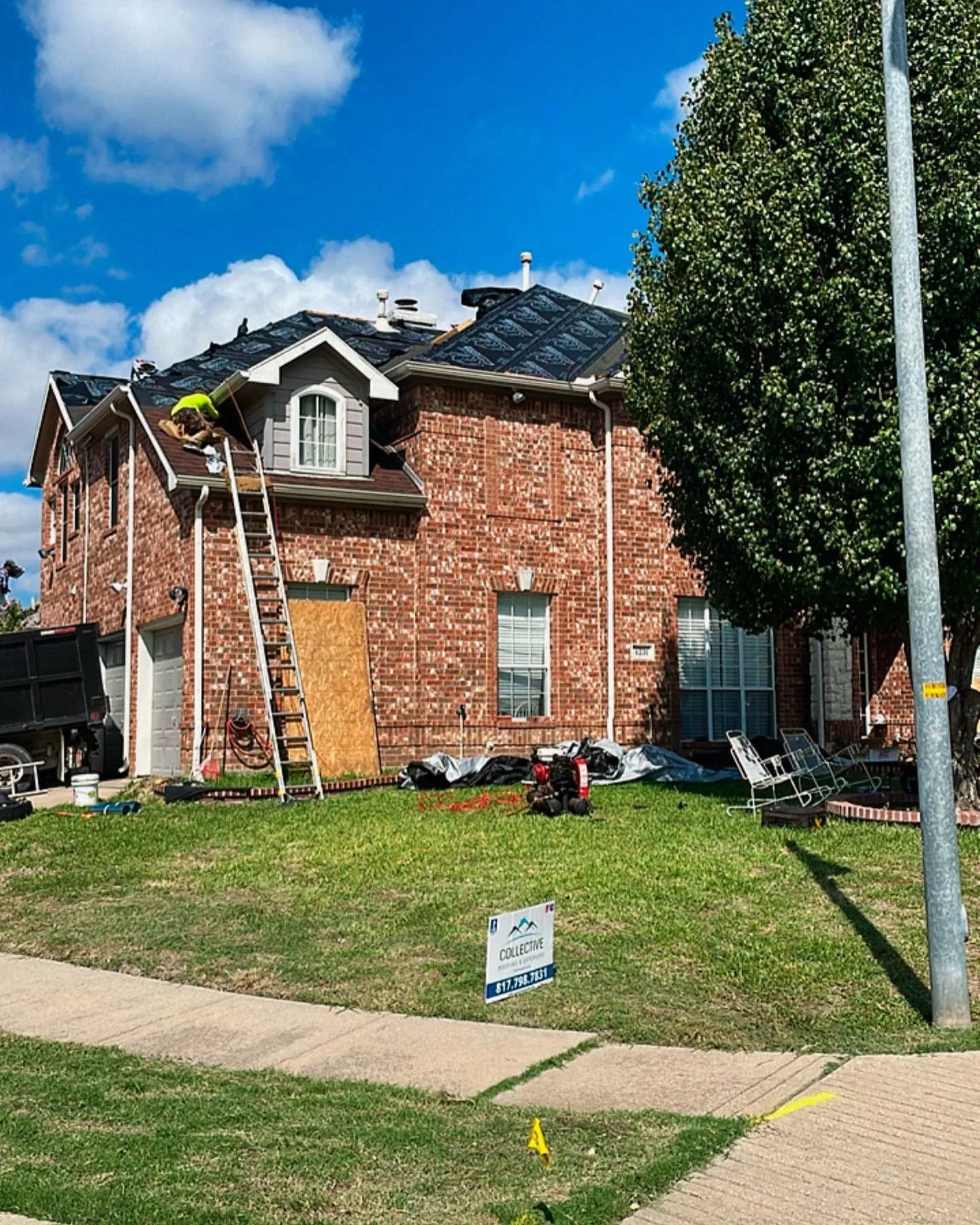 Two-story brick home with new dark shingle roof installation in progress, ladder and materials visible