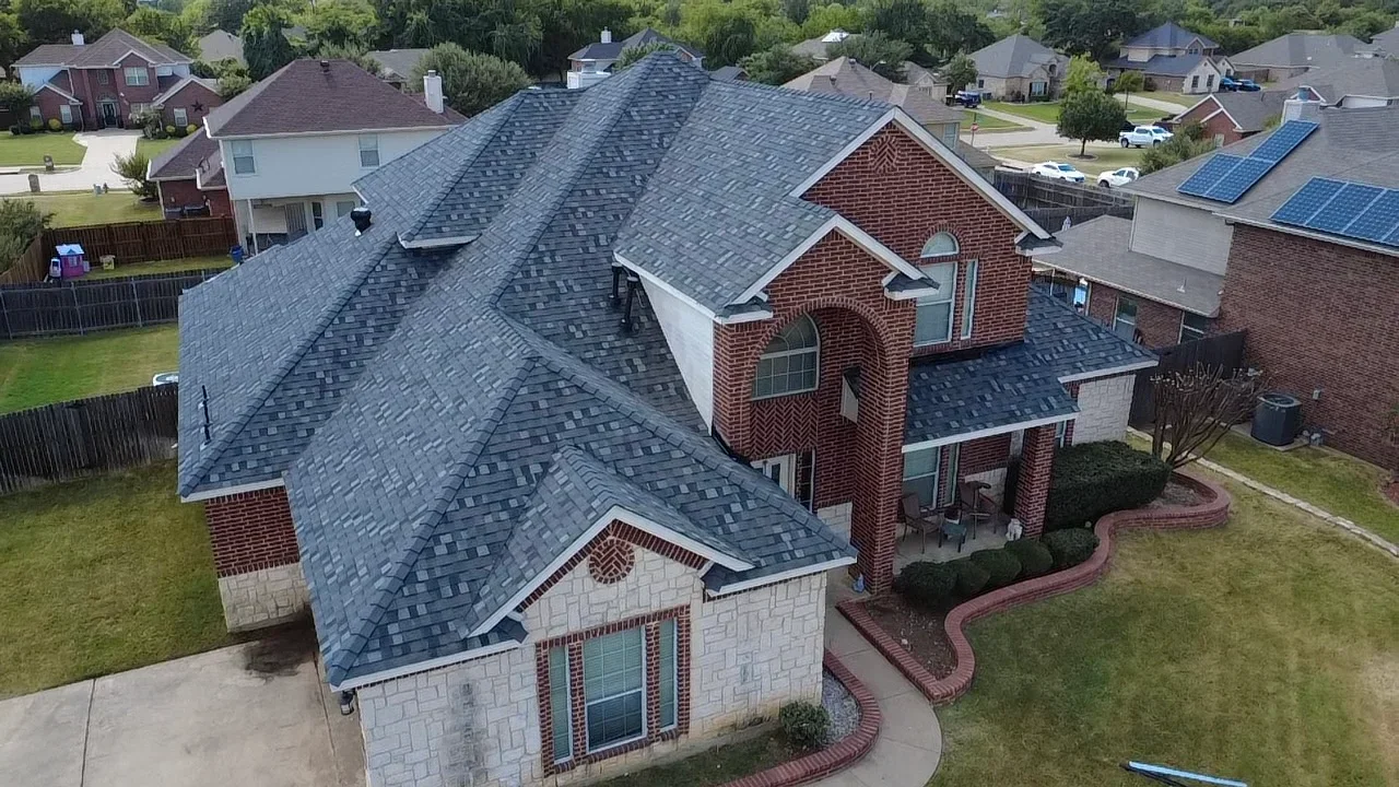 Aerial view of two-story brick home with new charcoal gray asphalt shingle roof installation