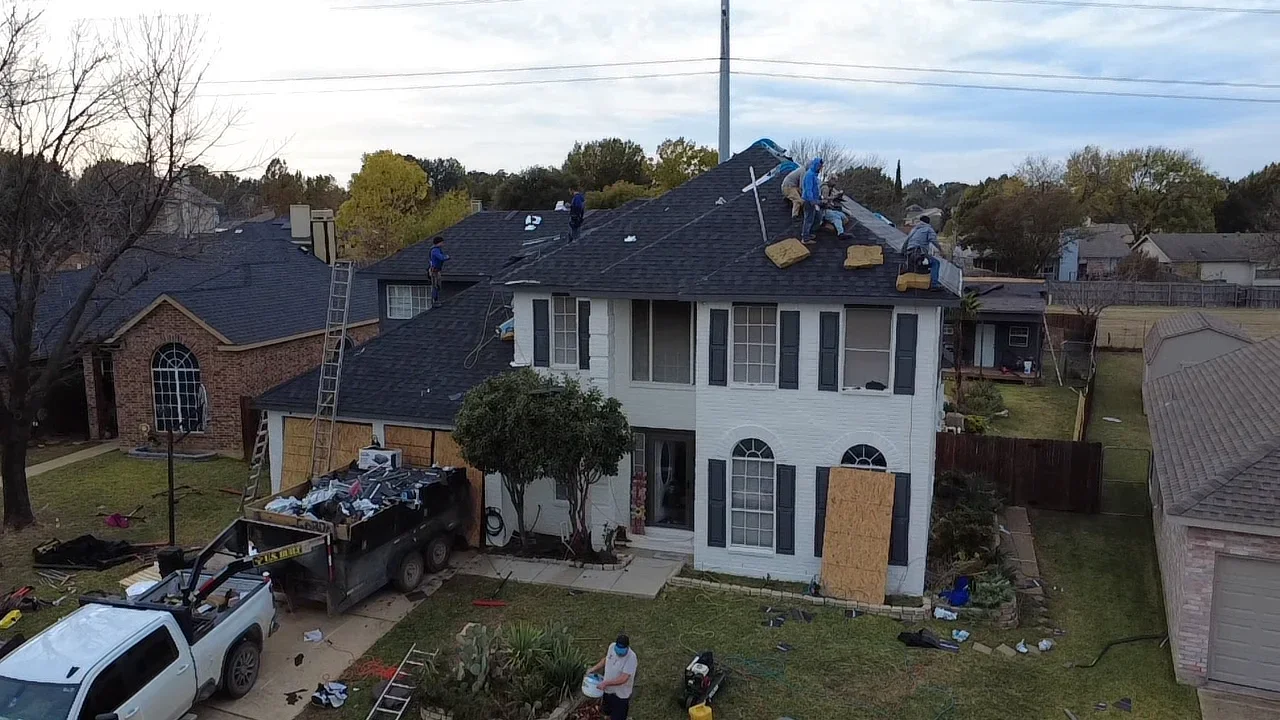 Two-story home with new dark asphalt shingle roof installation in progress, crews working on pitched roof planes