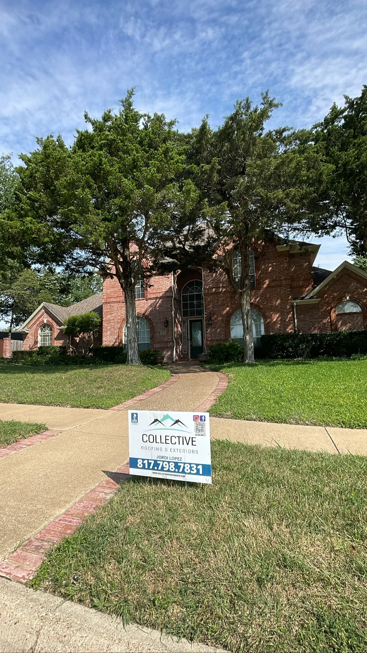 Two-story brick home with multi-plane roof, mature trees, and brick walkway