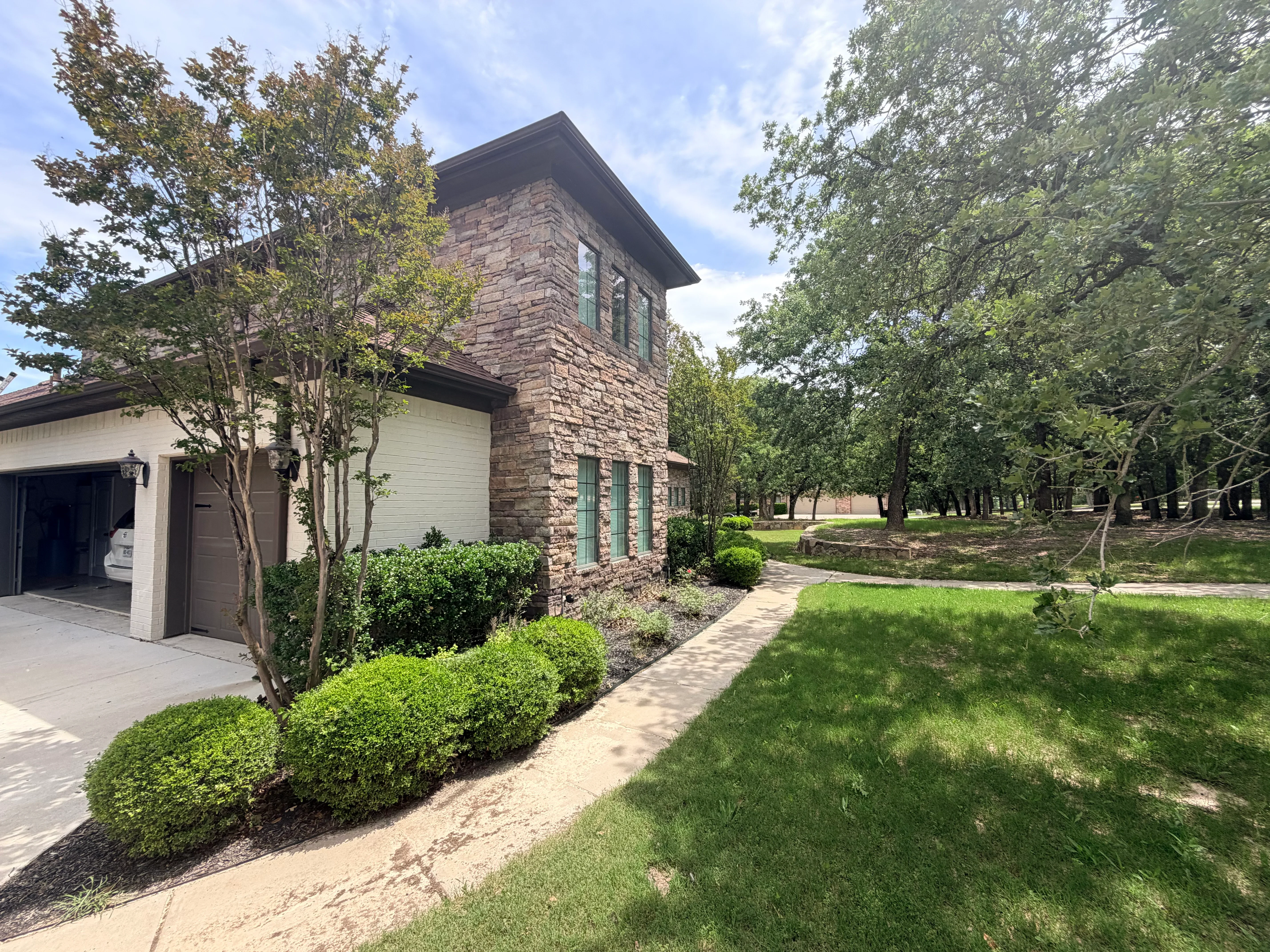 Stone and siding home with dark shingle roof, white garage, and manicured landscaping