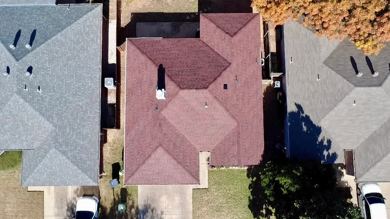 Aerial view of residential roofs with gray, burgundy, and tan asphalt shingles and multiple roof planes