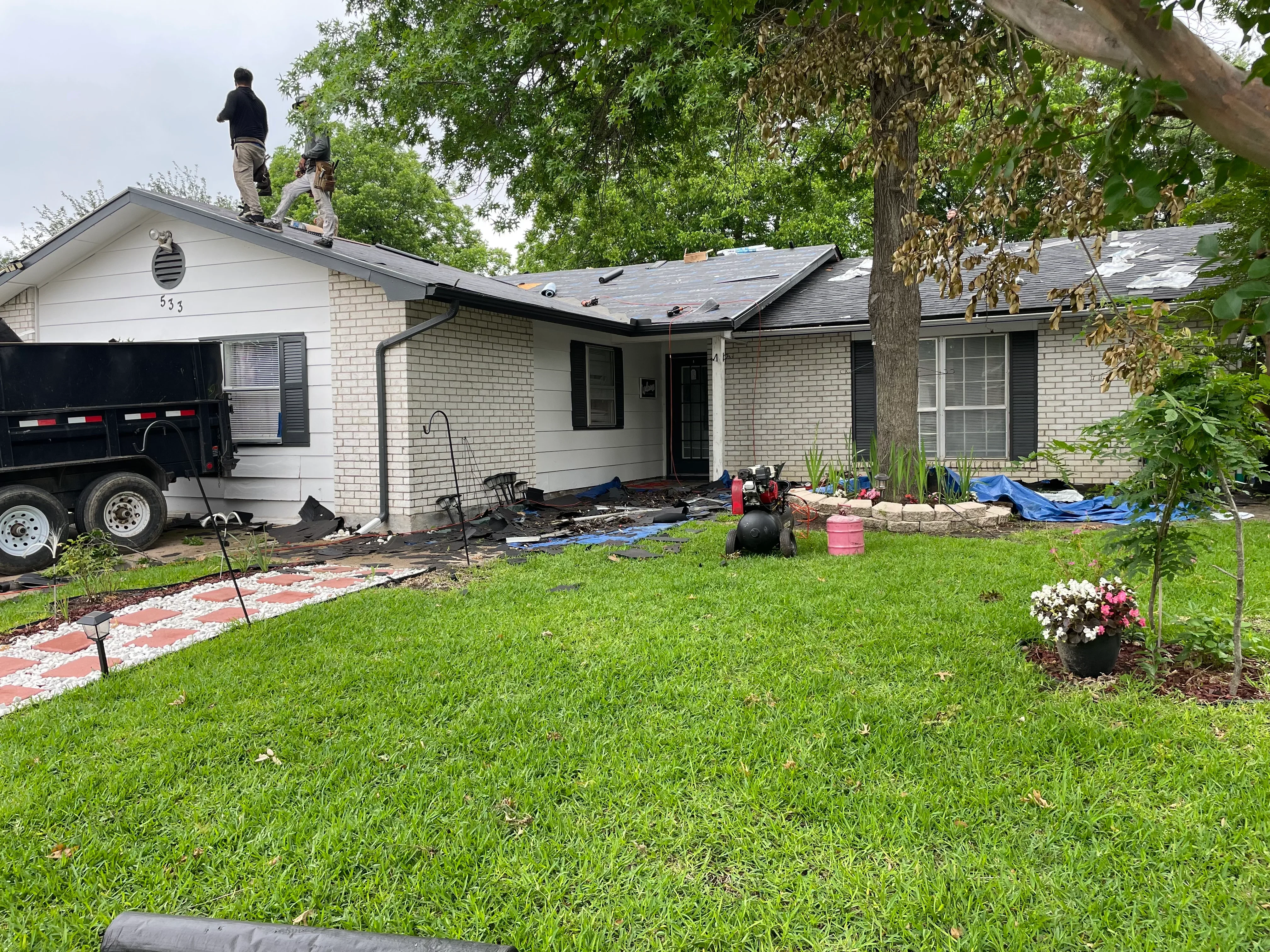 Roof replacement in progress on brick home with new asphalt shingles being installed