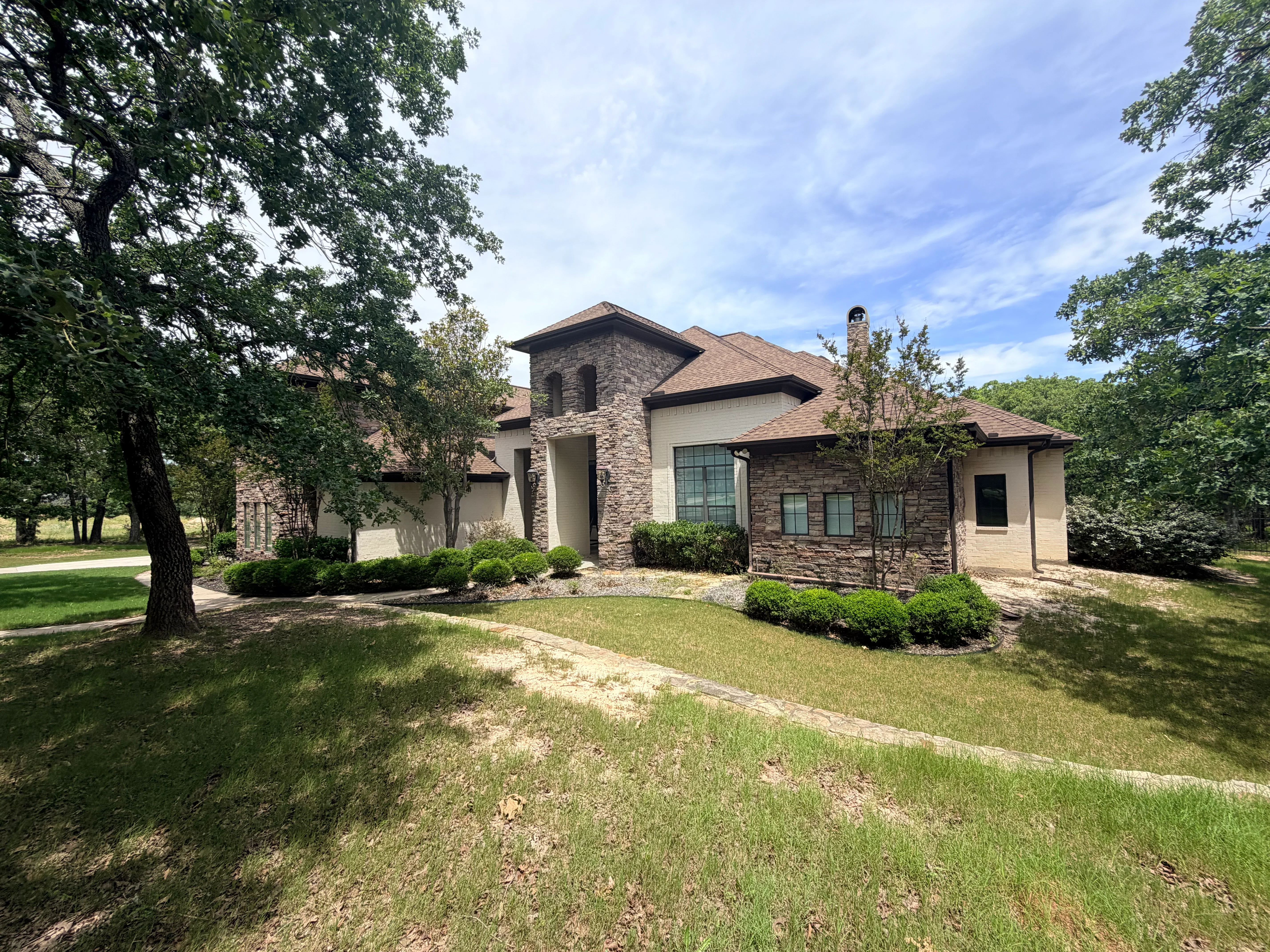 Two-story home with new brown architectural shingles, stone and stucco siding, gable roof design