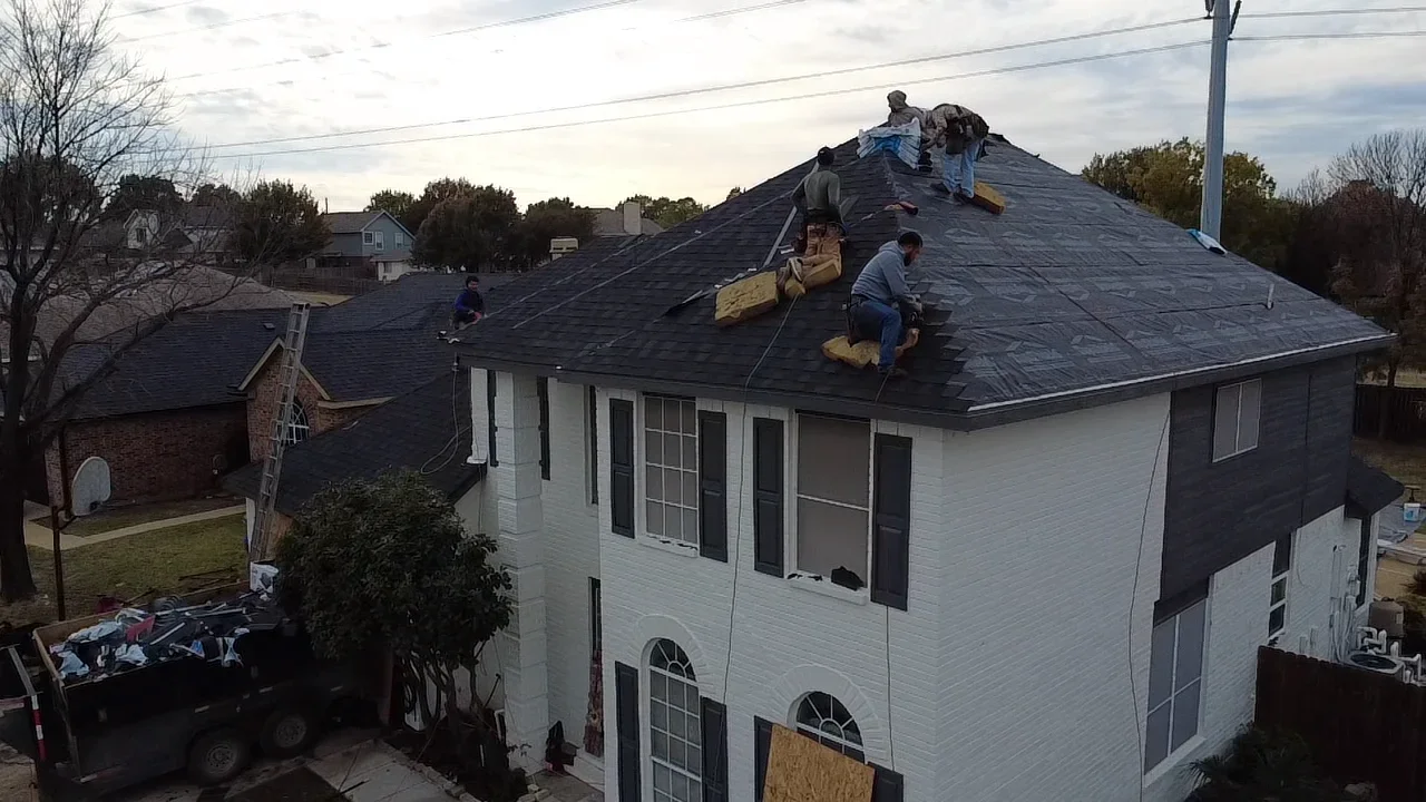 Roofers installing dark gray asphalt shingles on pitched residential roof with safety equipment