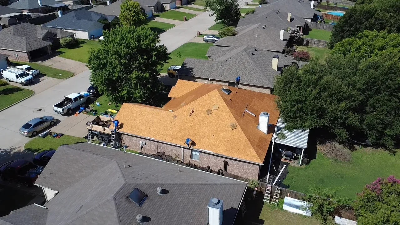 Aerial view of residential roof replacement with tan architectural shingles and worker on pitched roof