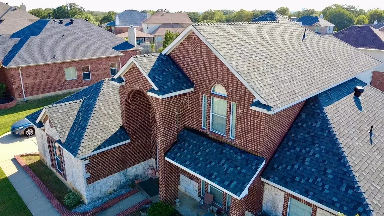 Aerial view of brick home with new blue-black asphalt shingle roof and white gutters