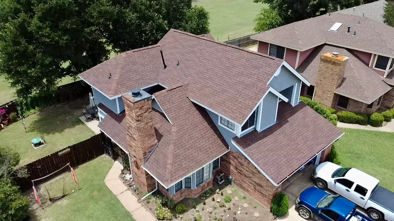 Aerial view of brick home with new brown architectural shingles, multiple roof sections, and brick chimneys