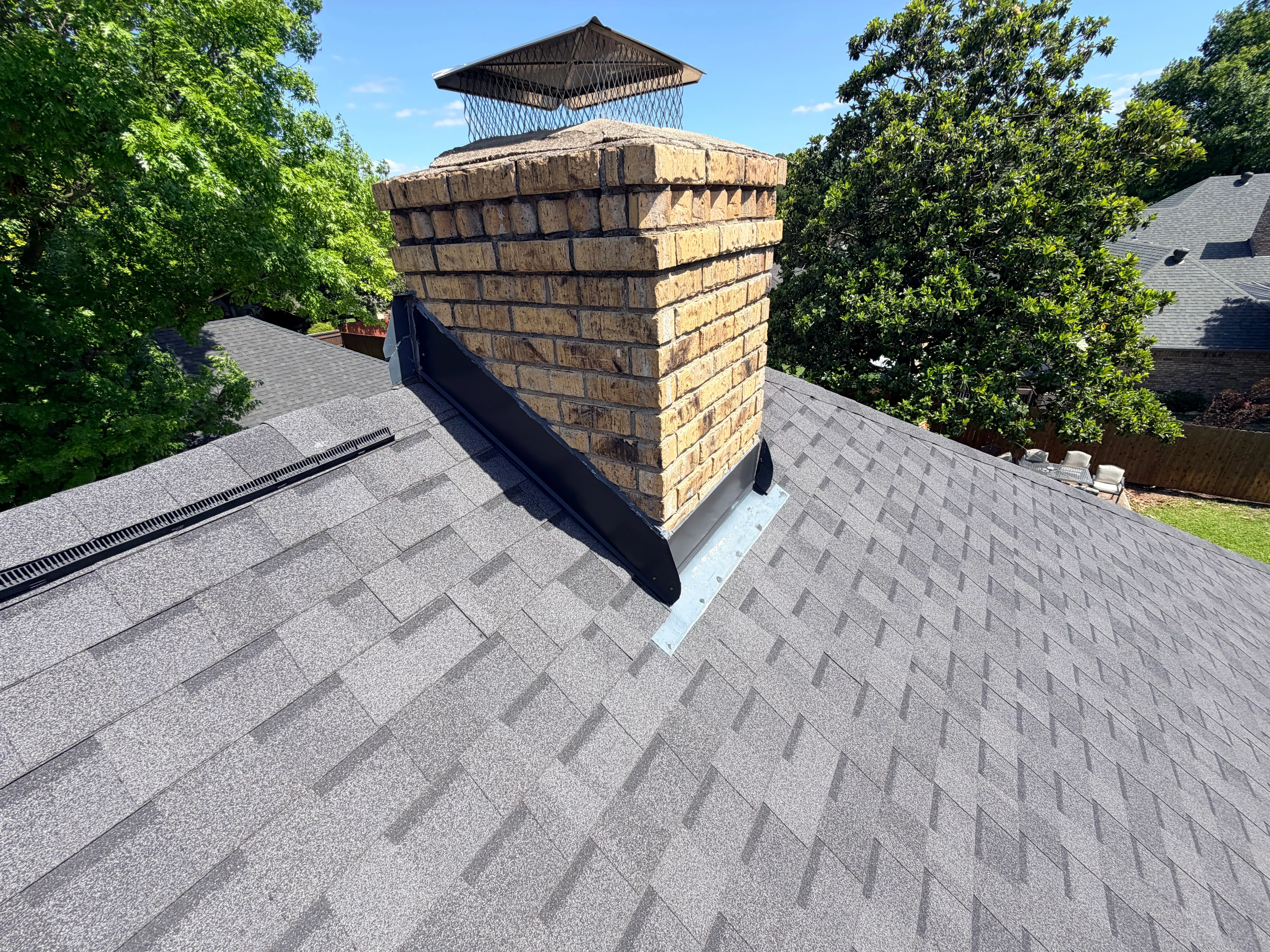 Gray architectural shingles with new chimney flashing and brick chimney on residential roof
