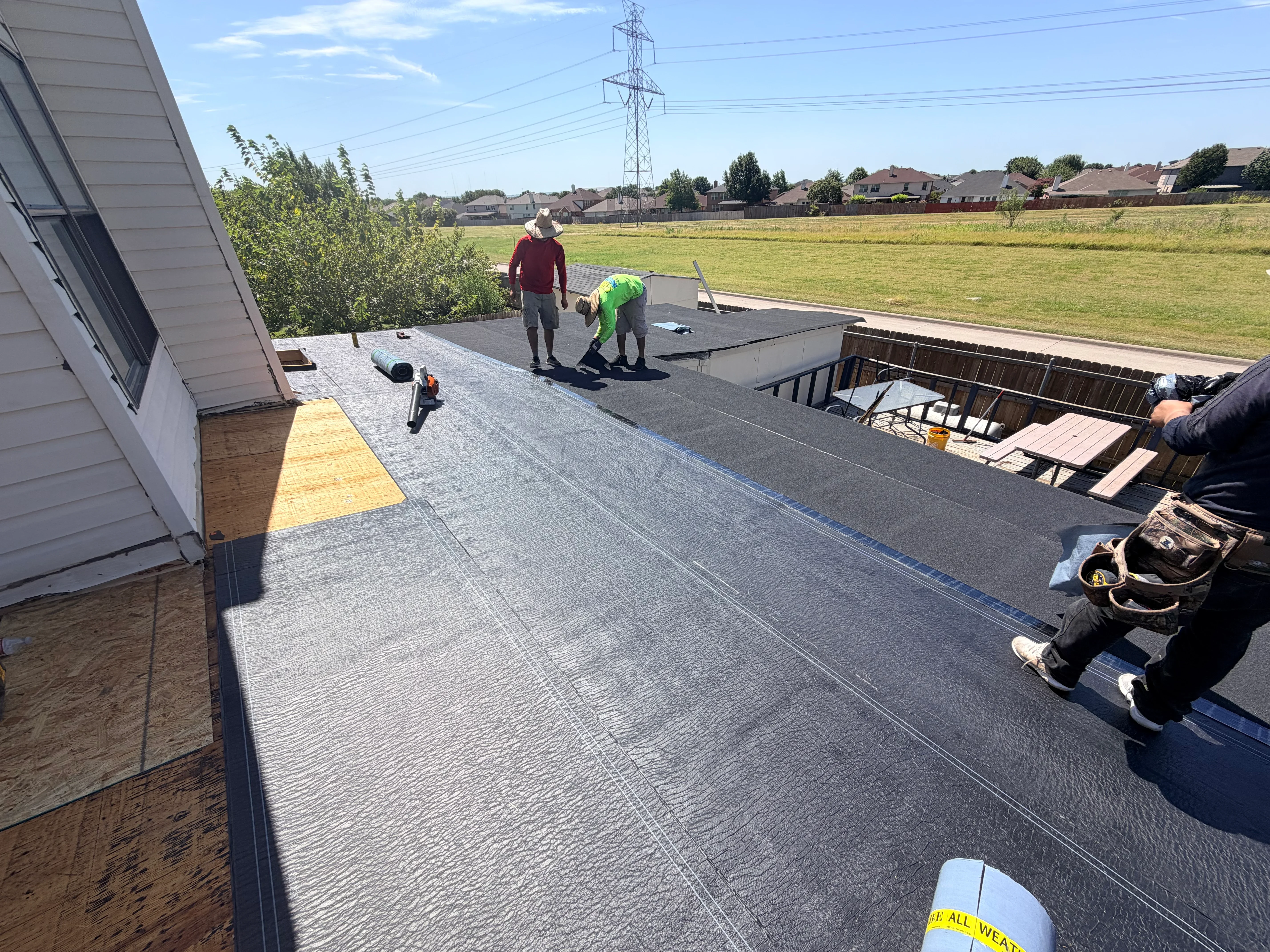 Roofers installing rolled asphalt membrane on residential flat roof with taped seams