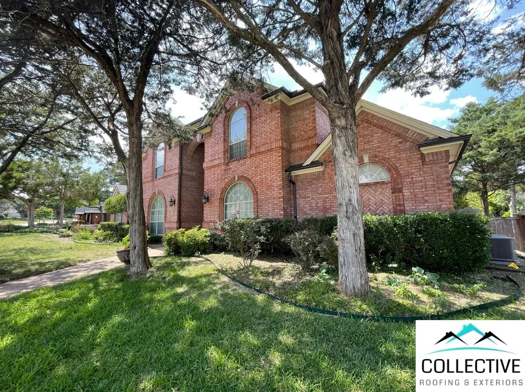 Two-story brick home with pitched roof, arched windows, and mature trees
