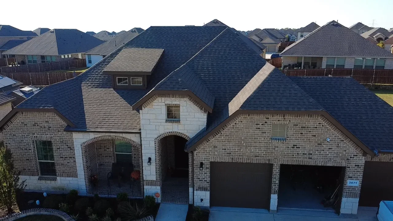 Dark architectural shingle roof installation on two-story brick home with multiple dormers and complex roof planes