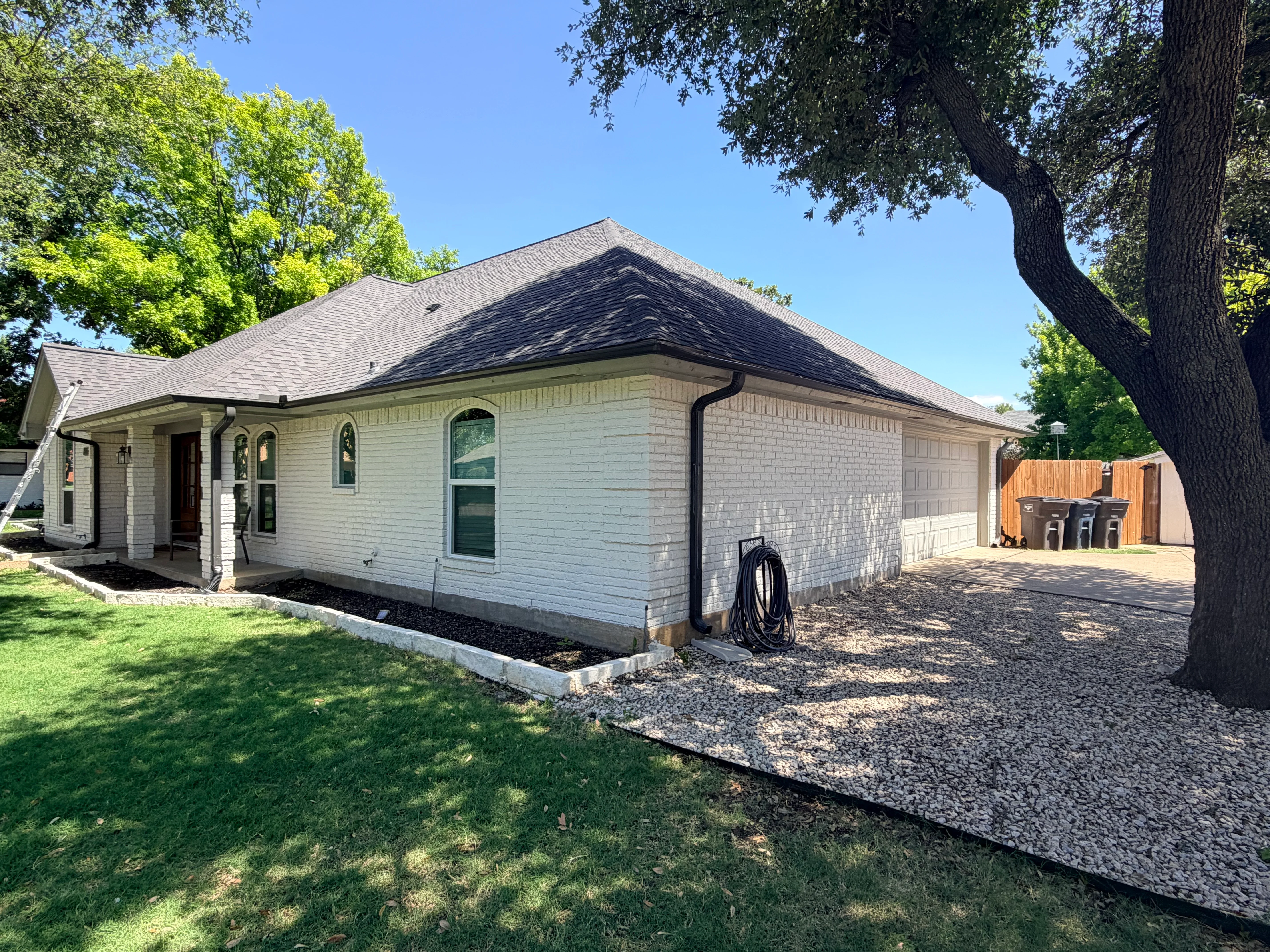 Charcoal gray architectural shingle roof with black gutters and downspouts on white brick home