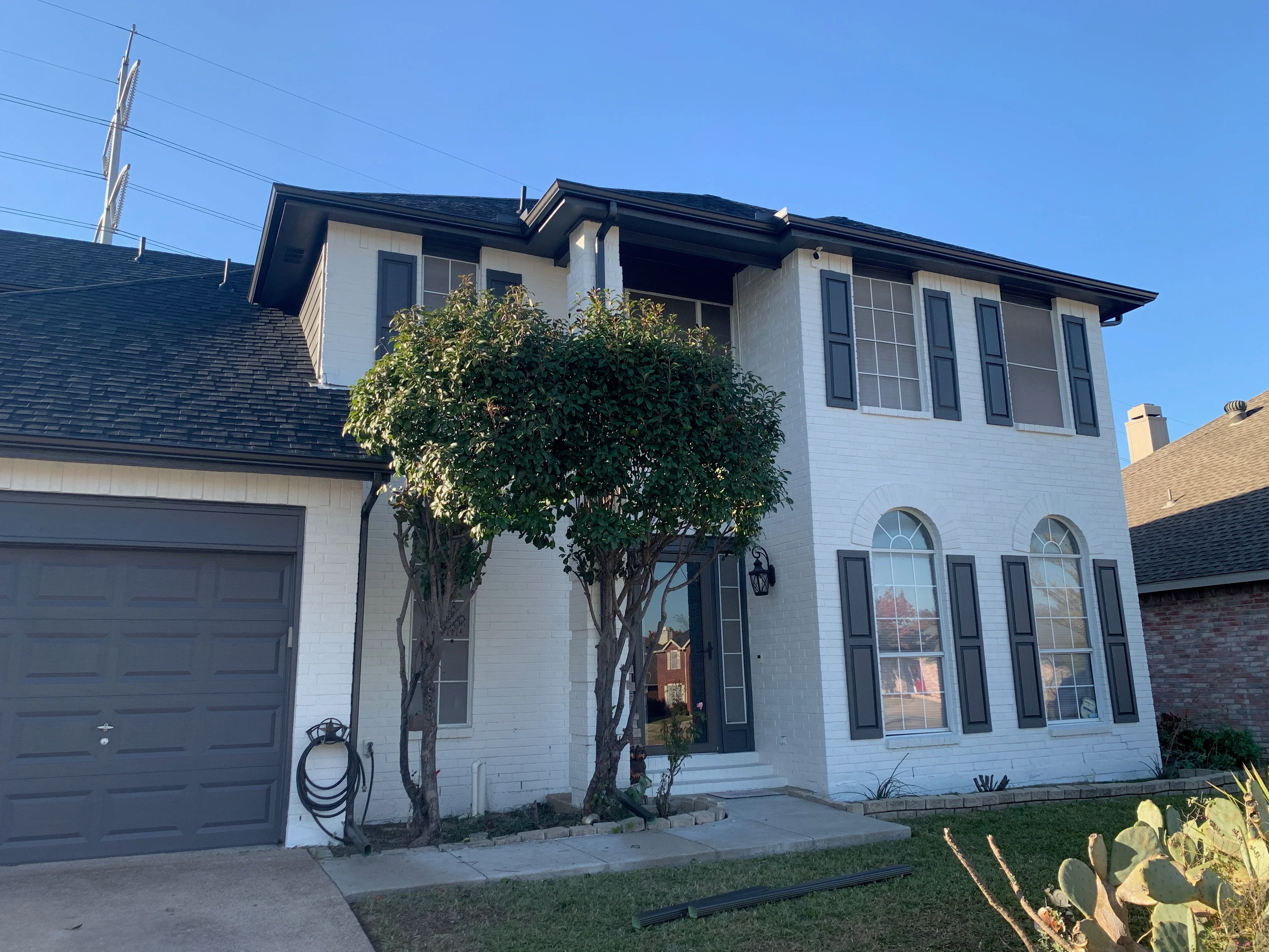 Dark asphalt shingle roof on two-story white brick home with multiple roof planes