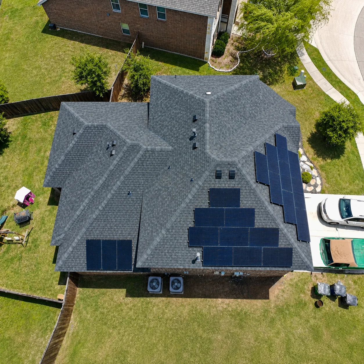 Aerial view of gray asphalt shingle roof with black solar panels installed on multiple slopes