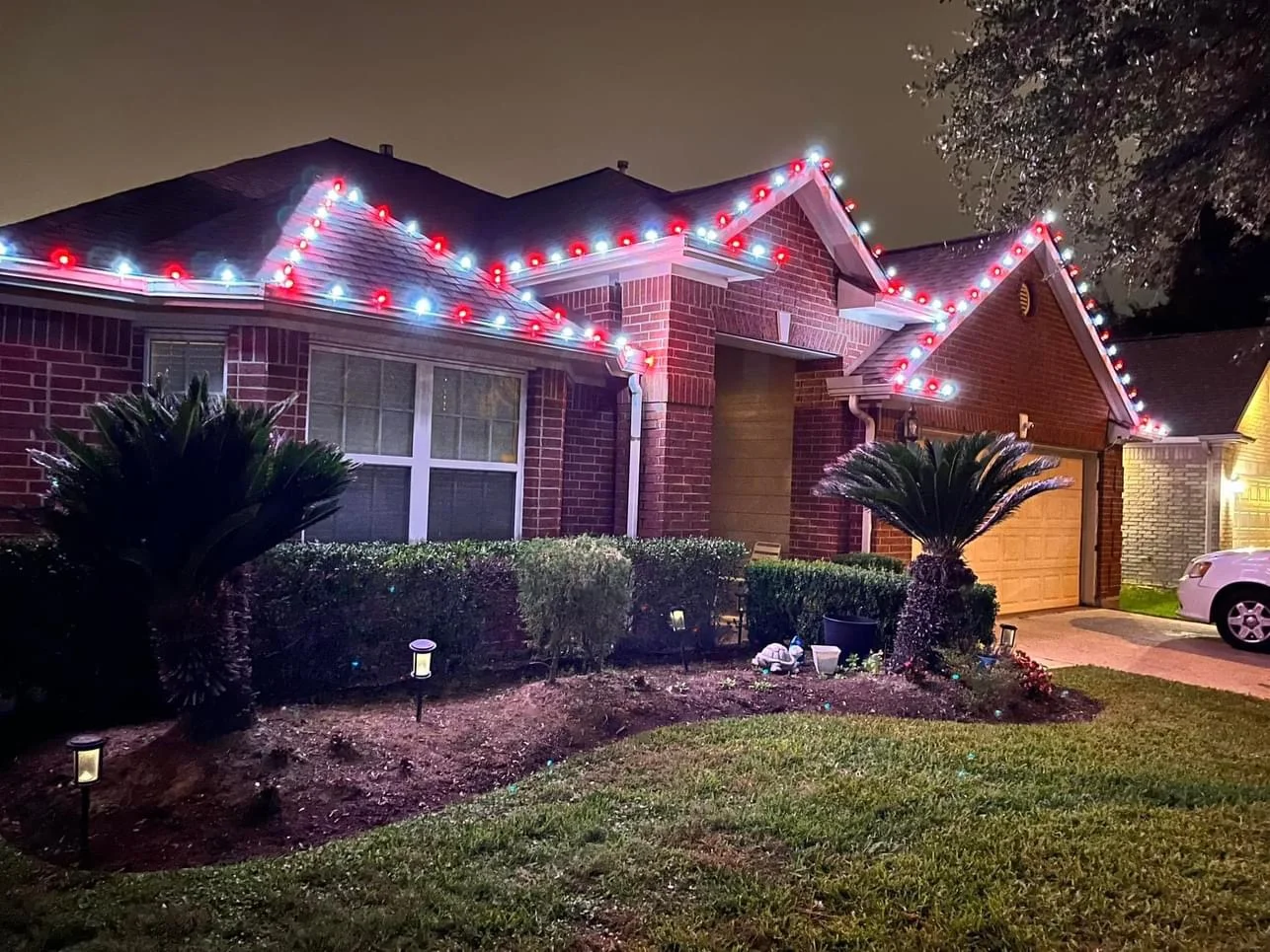 Professional holiday lighting installation on a brick home with red and white lights along the roofline at night